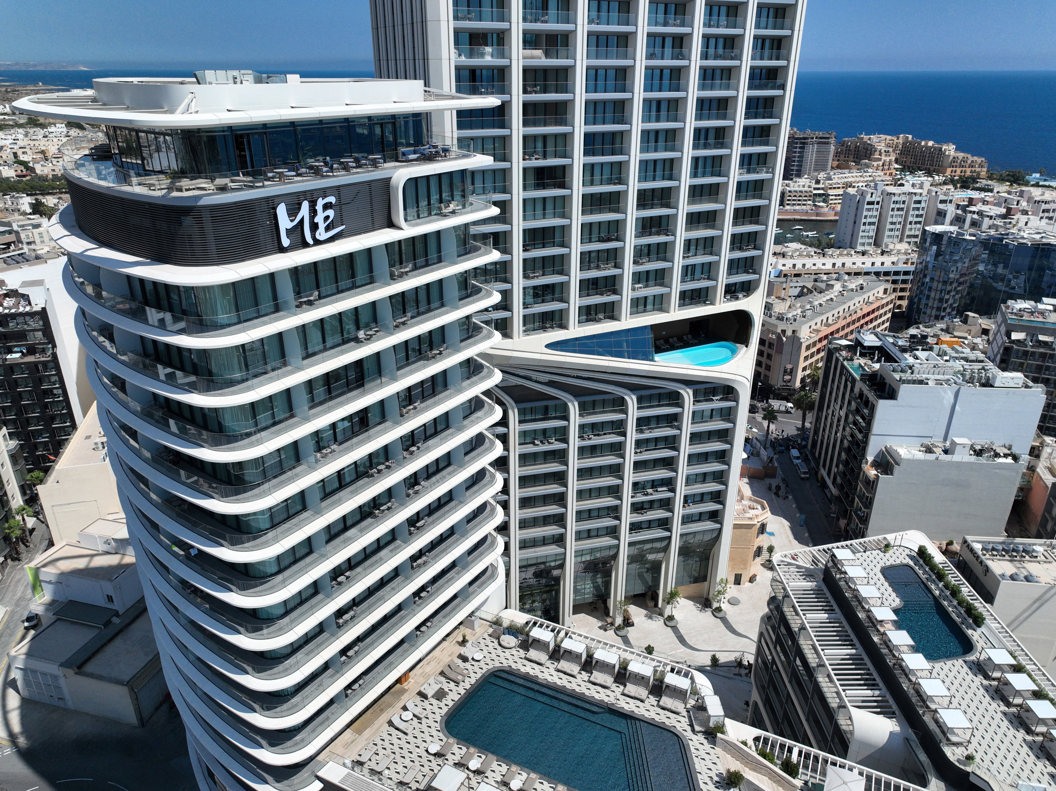 Modern ME hotel with curved architecture, rooftop pool, city, and sea views.