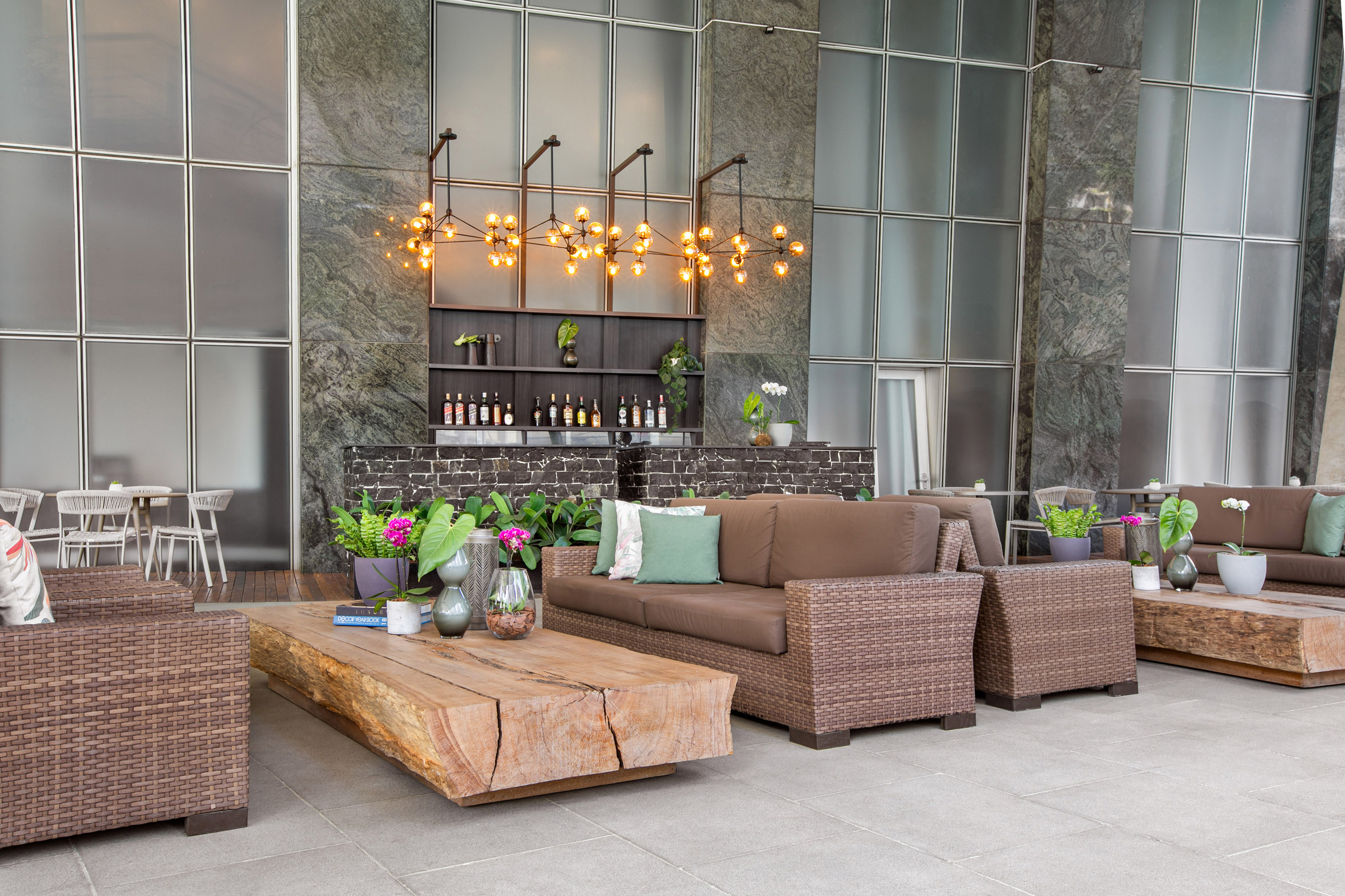 Luxury patio lounge with brown wicker furniture, unique wood table, and bar.