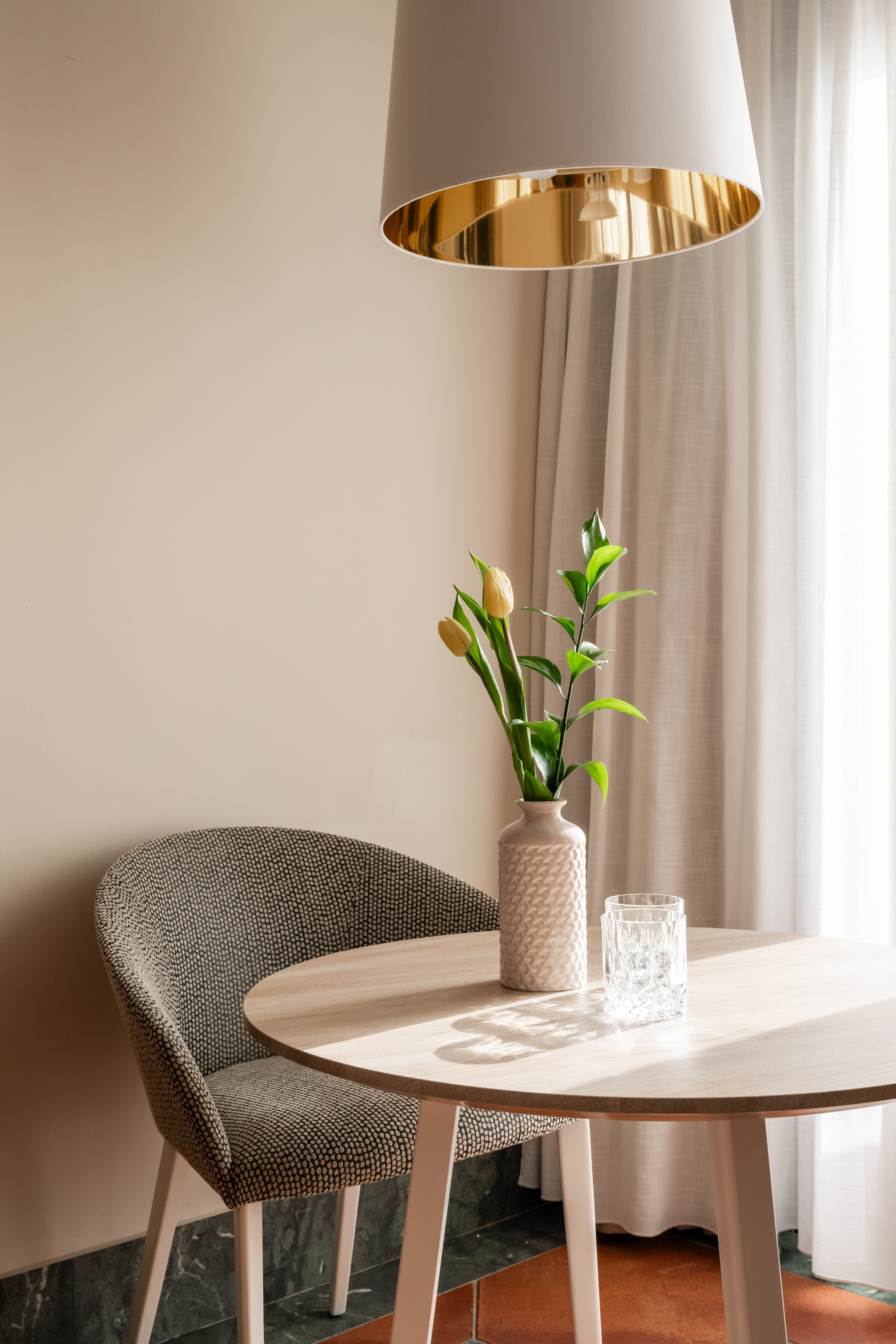 Modern dining table with yellow tulips, textured chair, and gold pendant light.