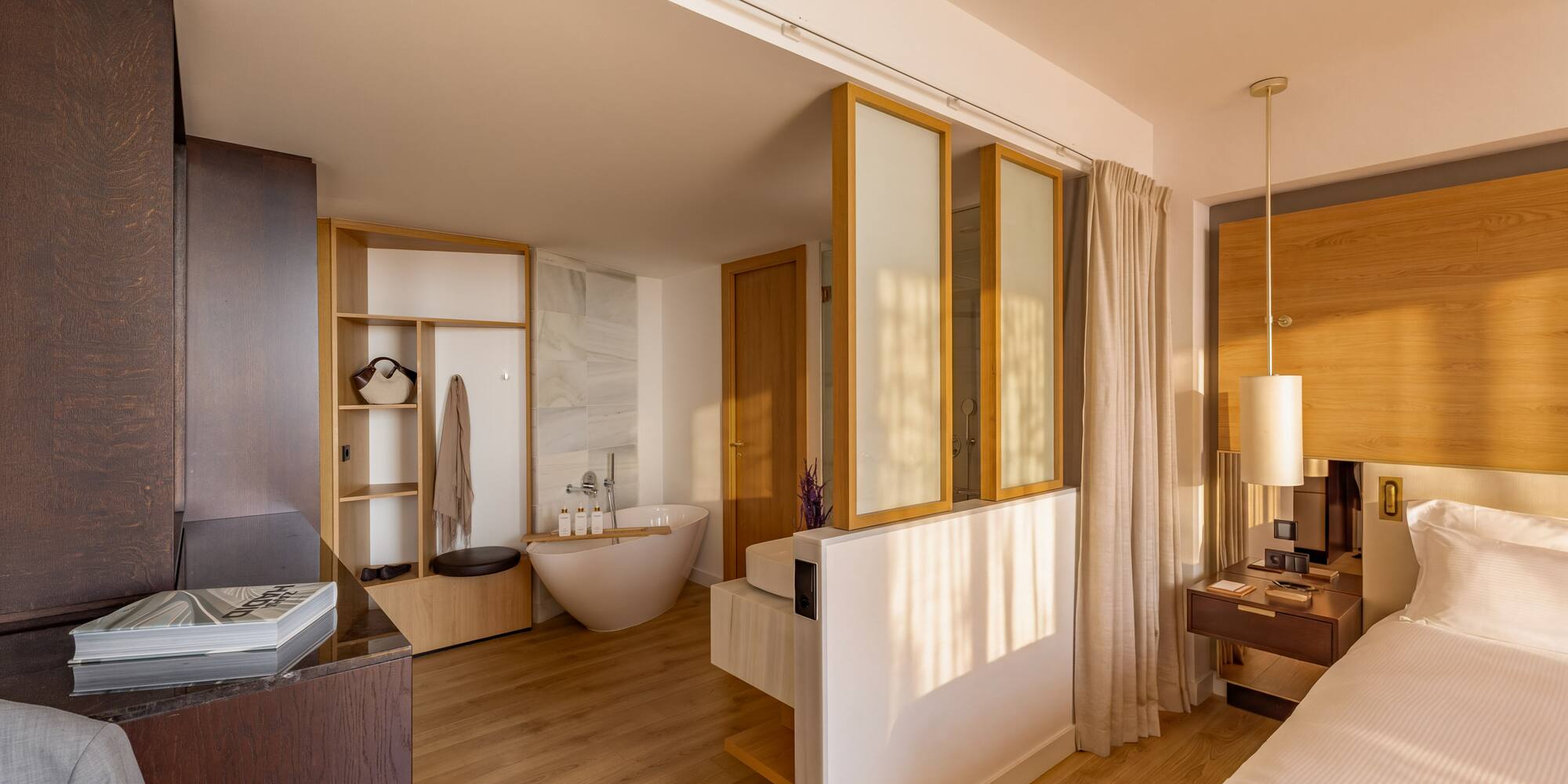 Modern hotel suite: bedroom with freestanding tub and open-concept bathroom.