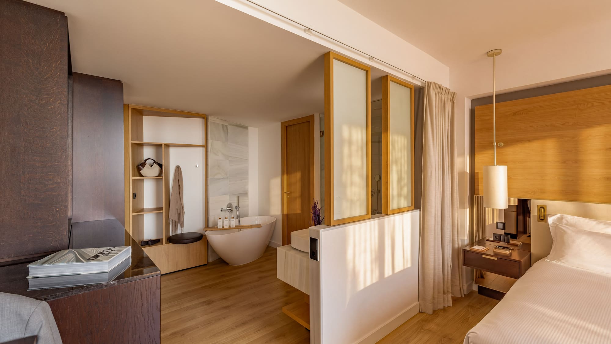 Modern hotel suite: bedroom with freestanding tub and open-concept bathroom.
