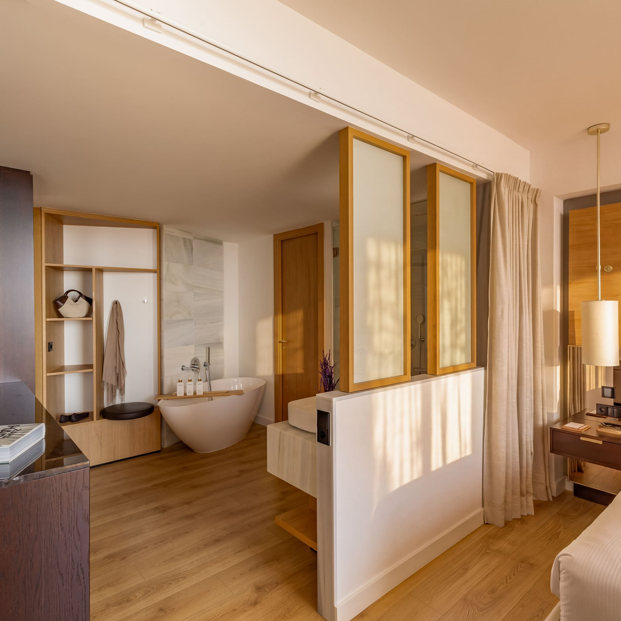 Modern hotel suite: bedroom with freestanding tub and open-concept bathroom.