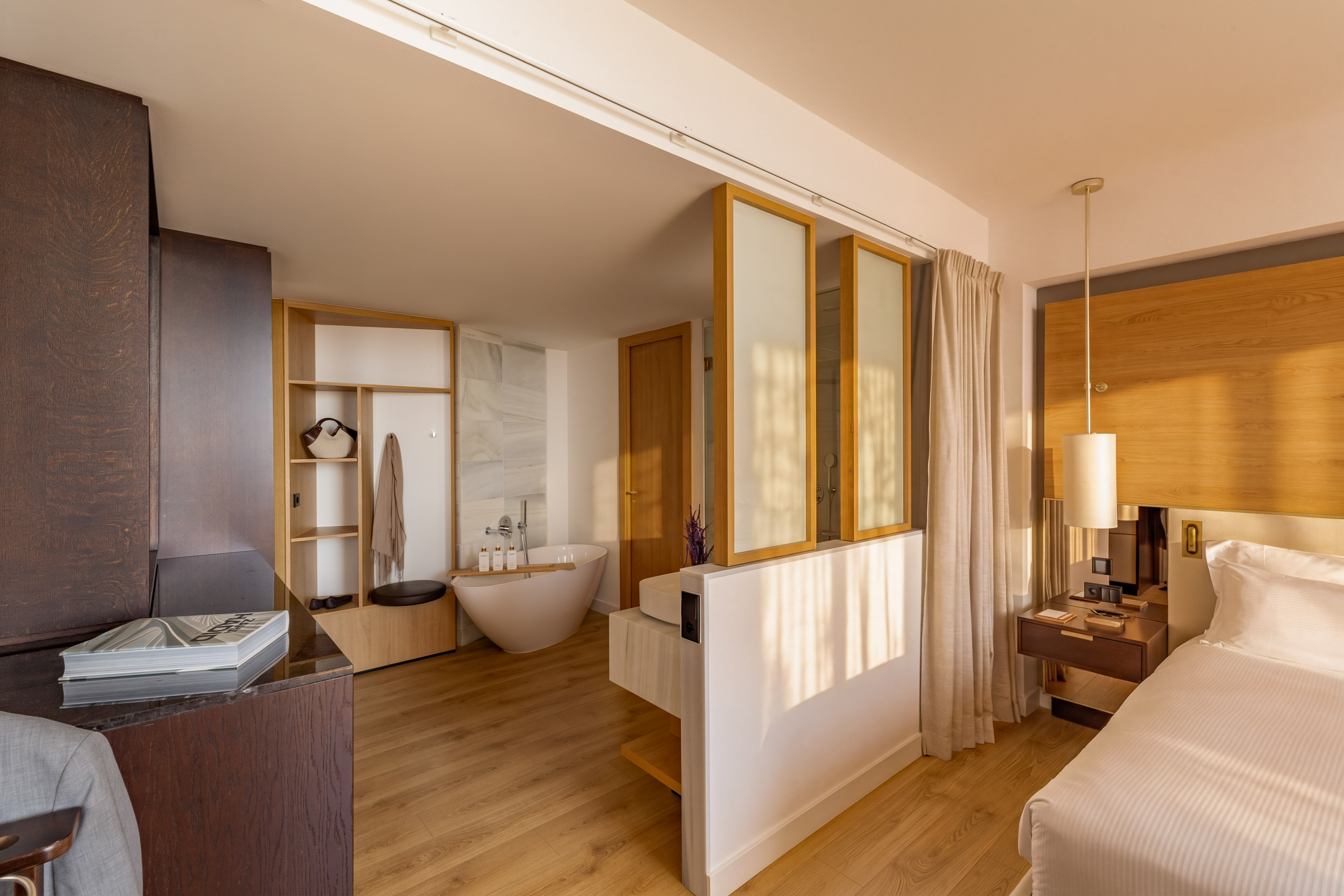 Modern hotel suite: bedroom with freestanding tub and open-concept bathroom.