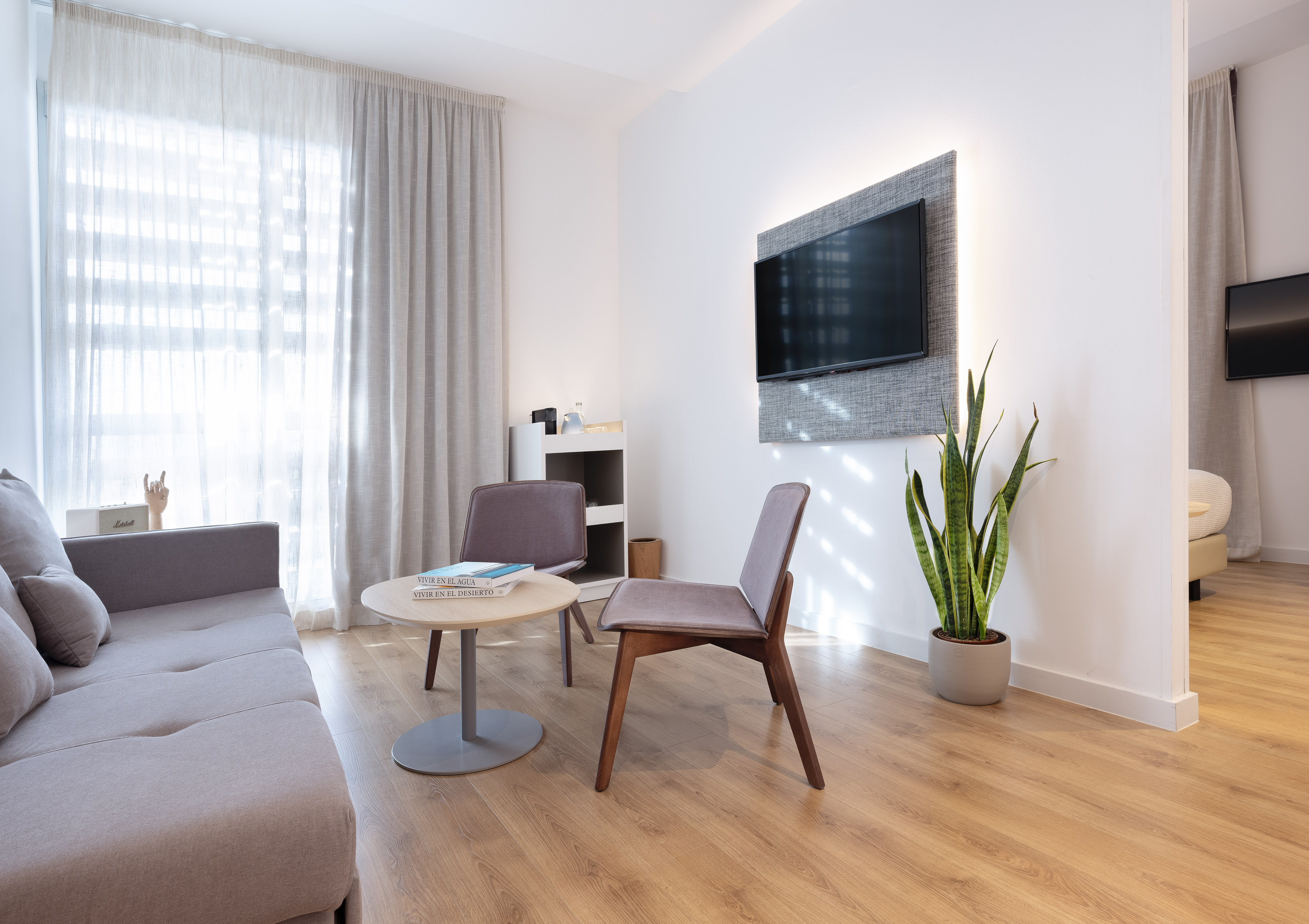 Grey sofa, modern chairs, backlit TV, wood floor, bright window.