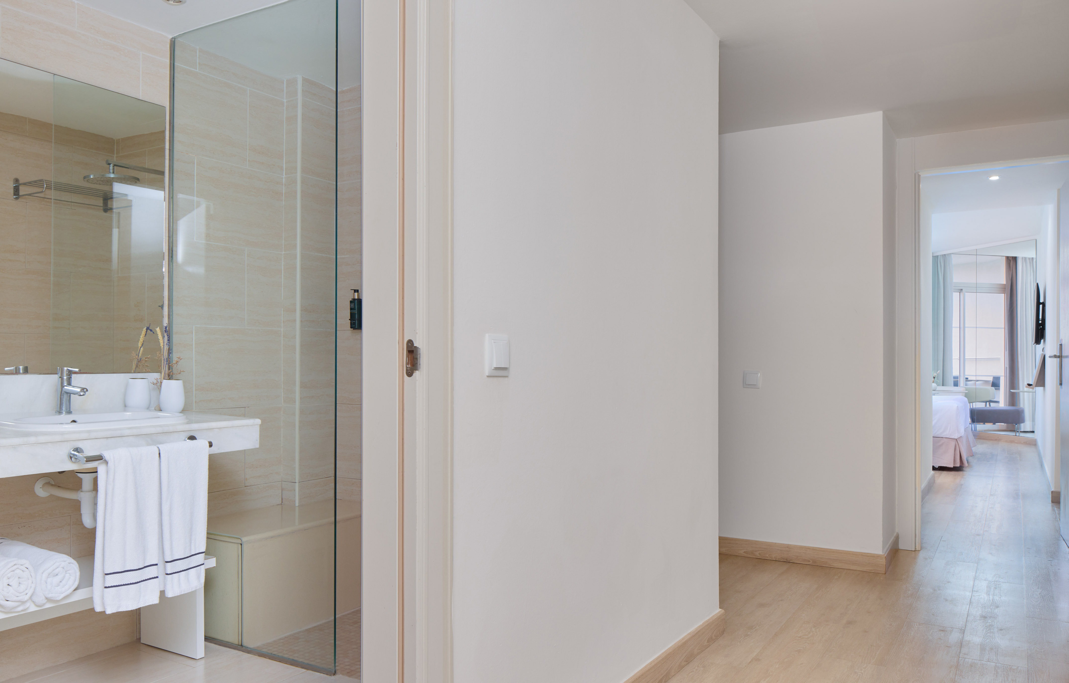 Modern hotel bathroom with glass shower, vanity, and bedroom view.