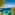 Pine-framed Mediterranean bay: clear turquoise water, boats, and distant cliffs.