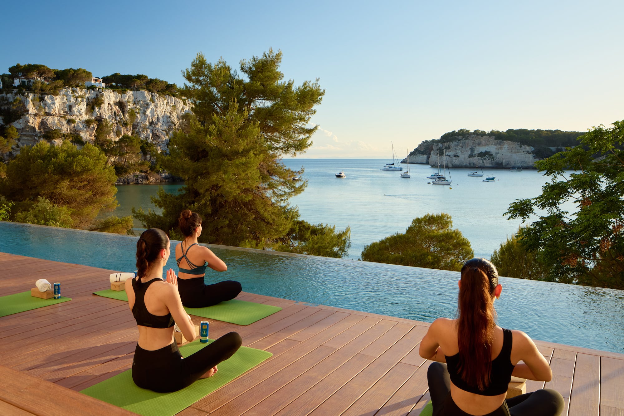 a group of women sitting on mats by a pool with water and boats