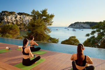 a group of women sitting on mats by a pool with water and boats