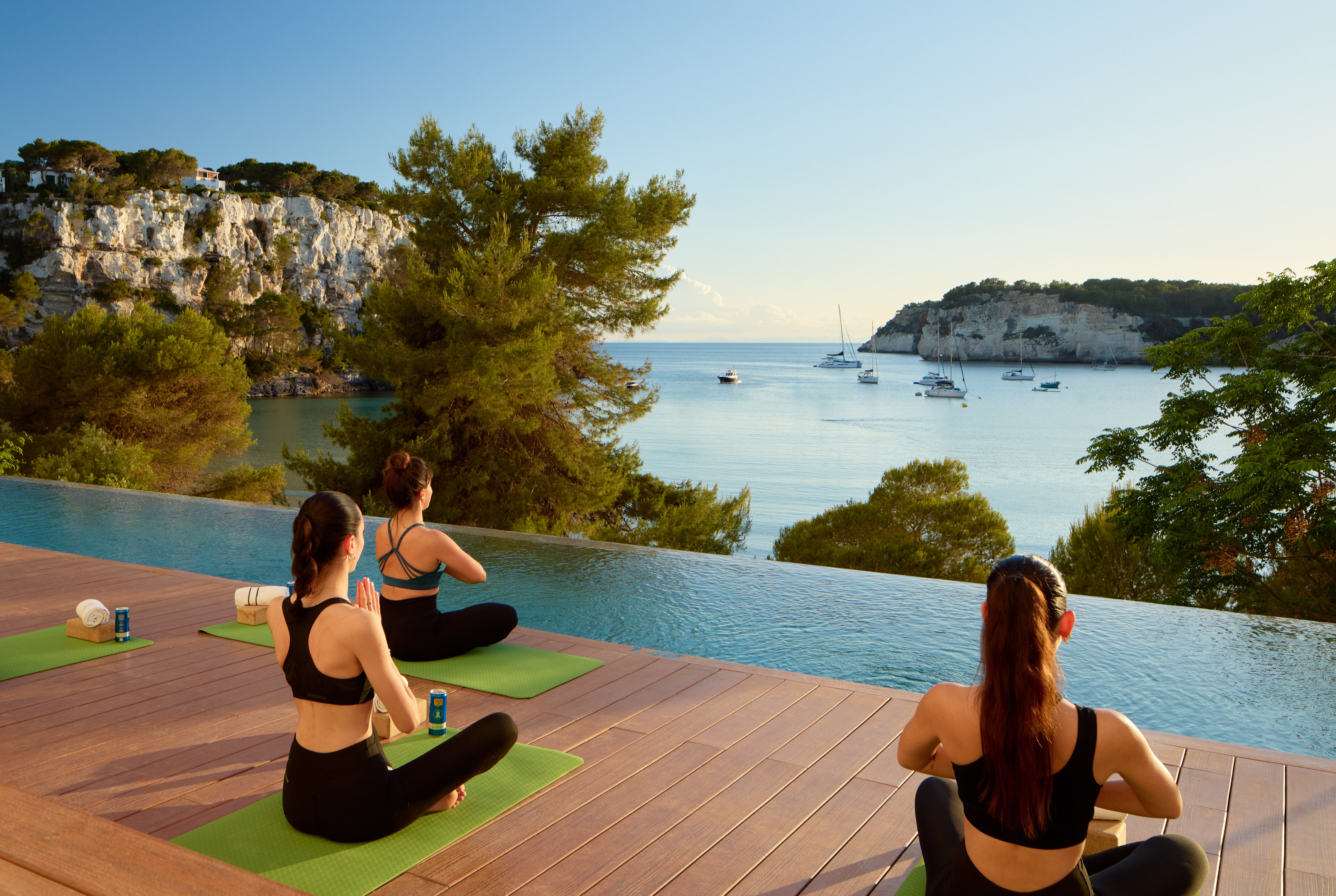 a group of women sitting on mats by a pool with water and boats