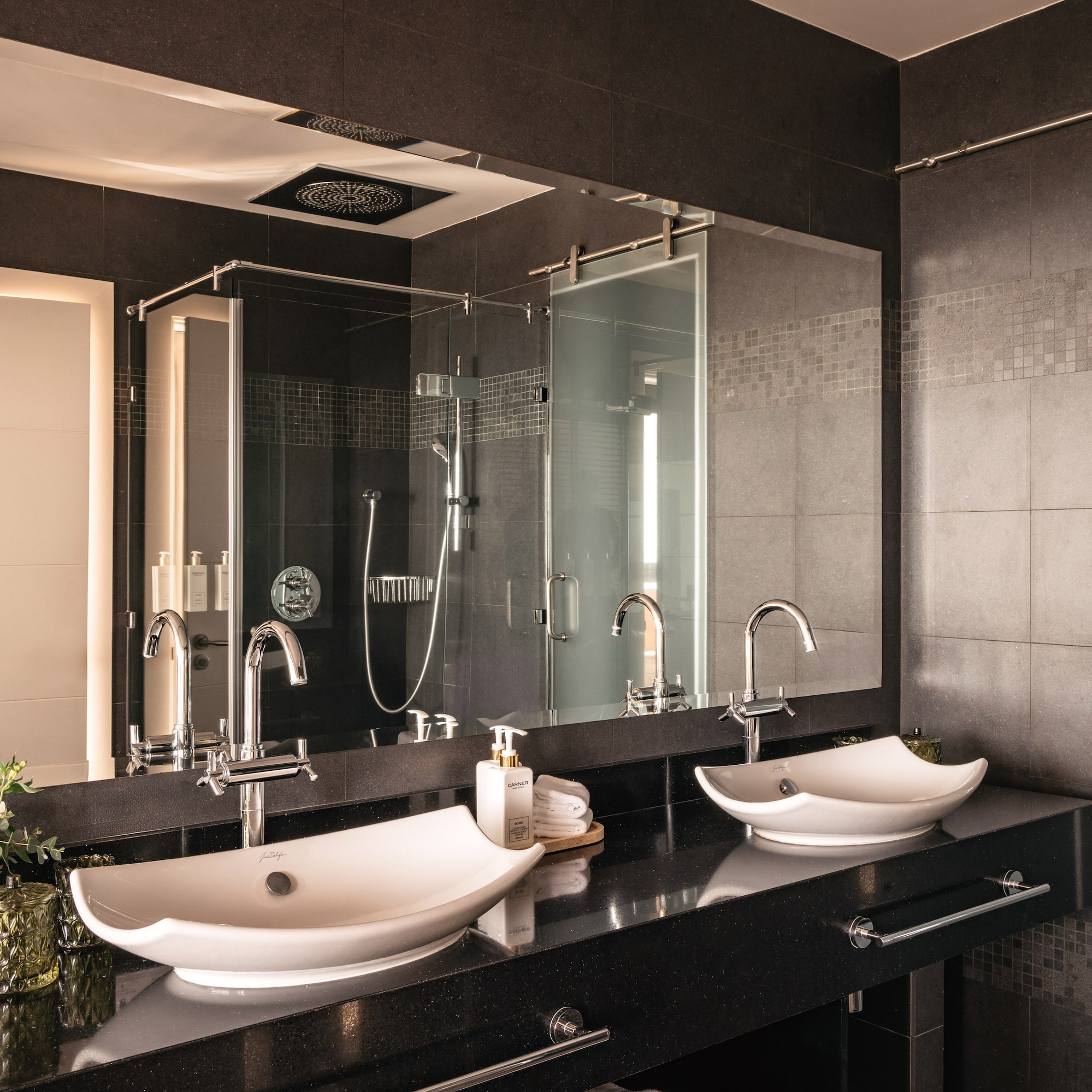 Modern luxury bathroom with double vessel sinks, black countertop, glass shower.