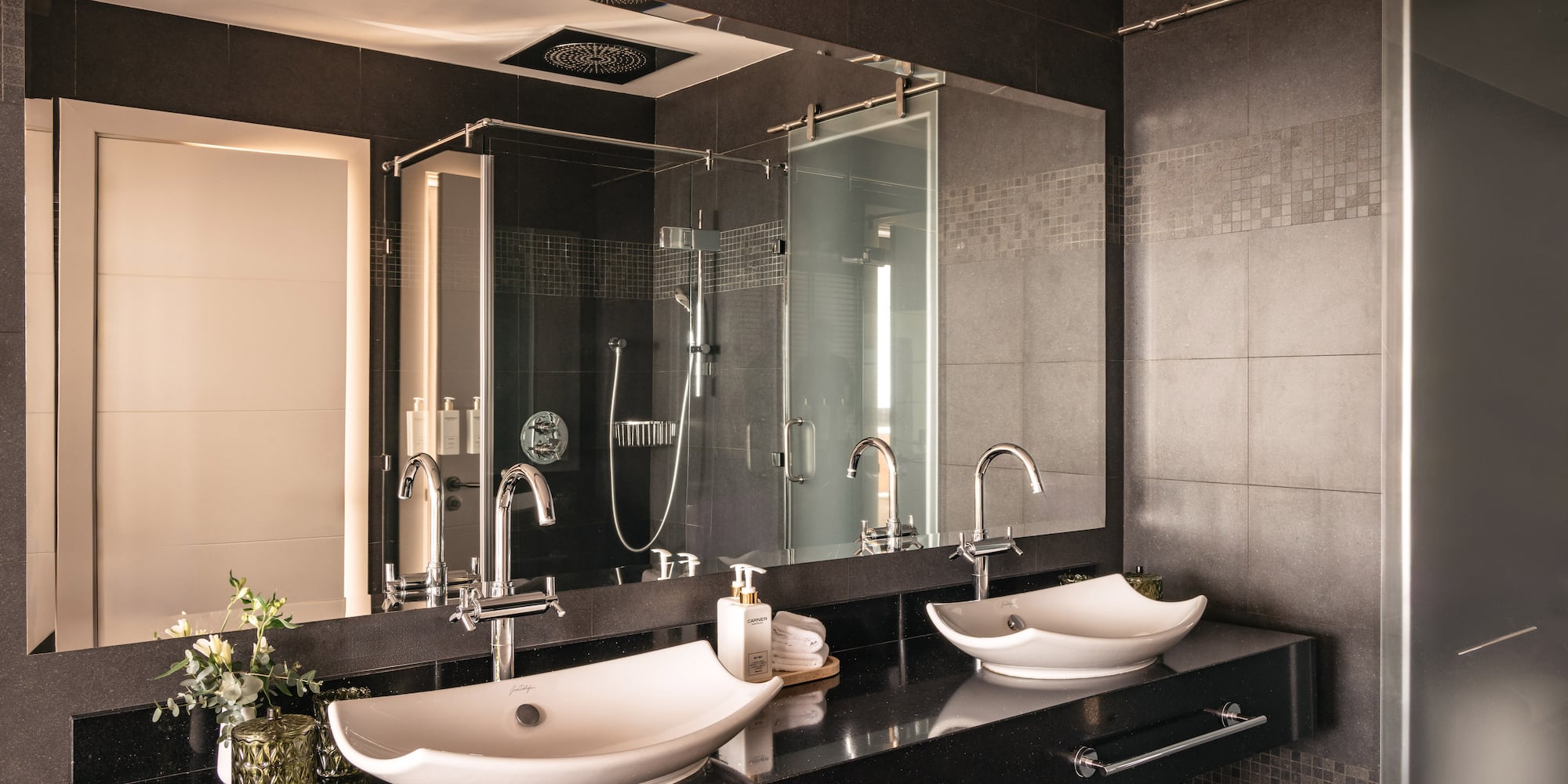 Modern luxury bathroom with double vessel sinks, black countertop, glass shower.