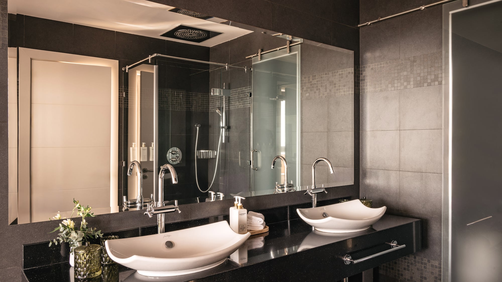Modern luxury bathroom with double vessel sinks, black countertop, glass shower.