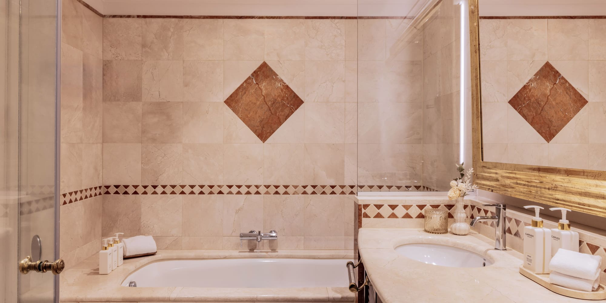 Luxurious marble bathroom with bathtub, double vanity, and gold mirror.