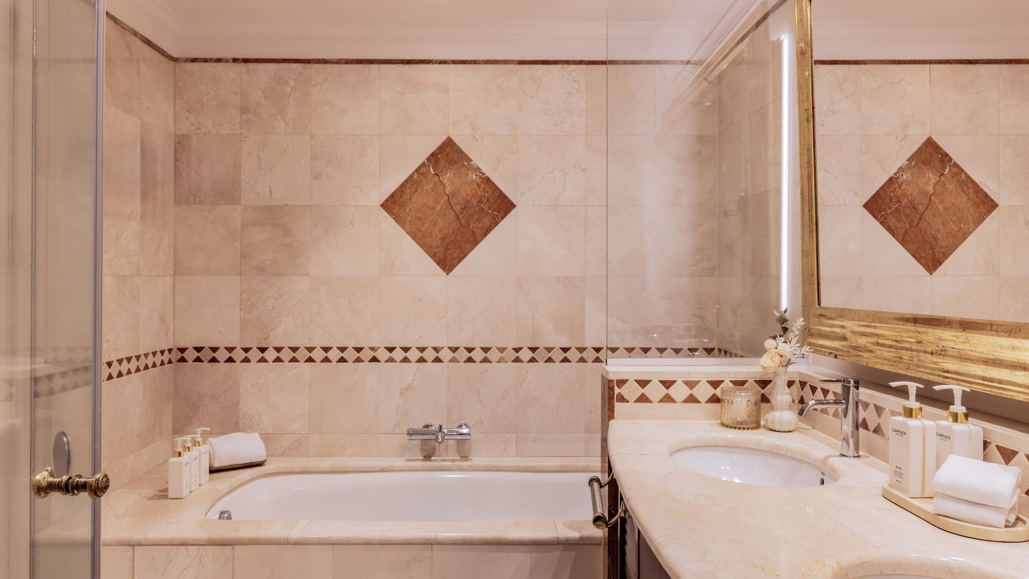 Luxurious marble bathroom with bathtub, double vanity, and gold mirror.