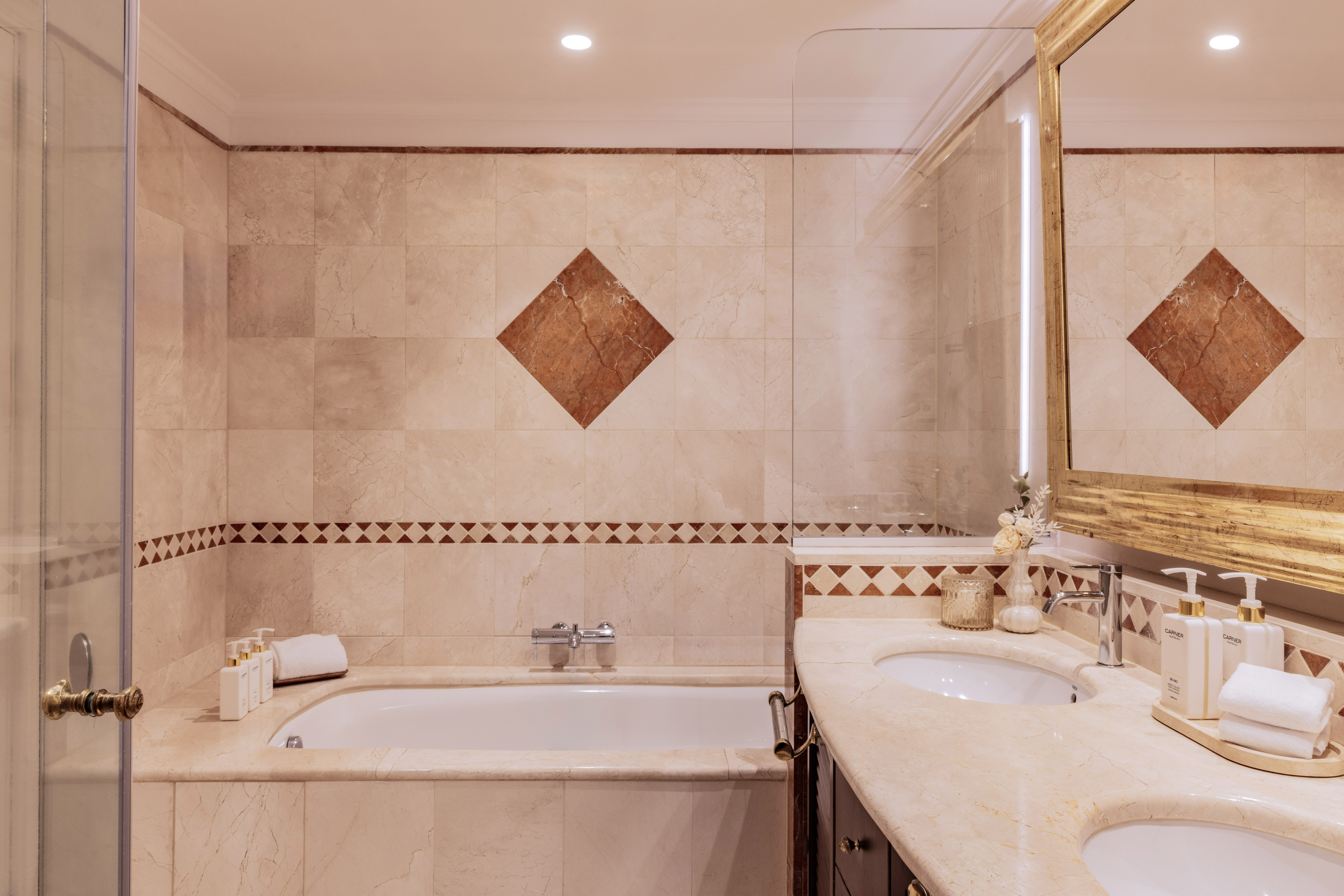 Luxurious marble bathroom with bathtub, double vanity, and gold mirror.