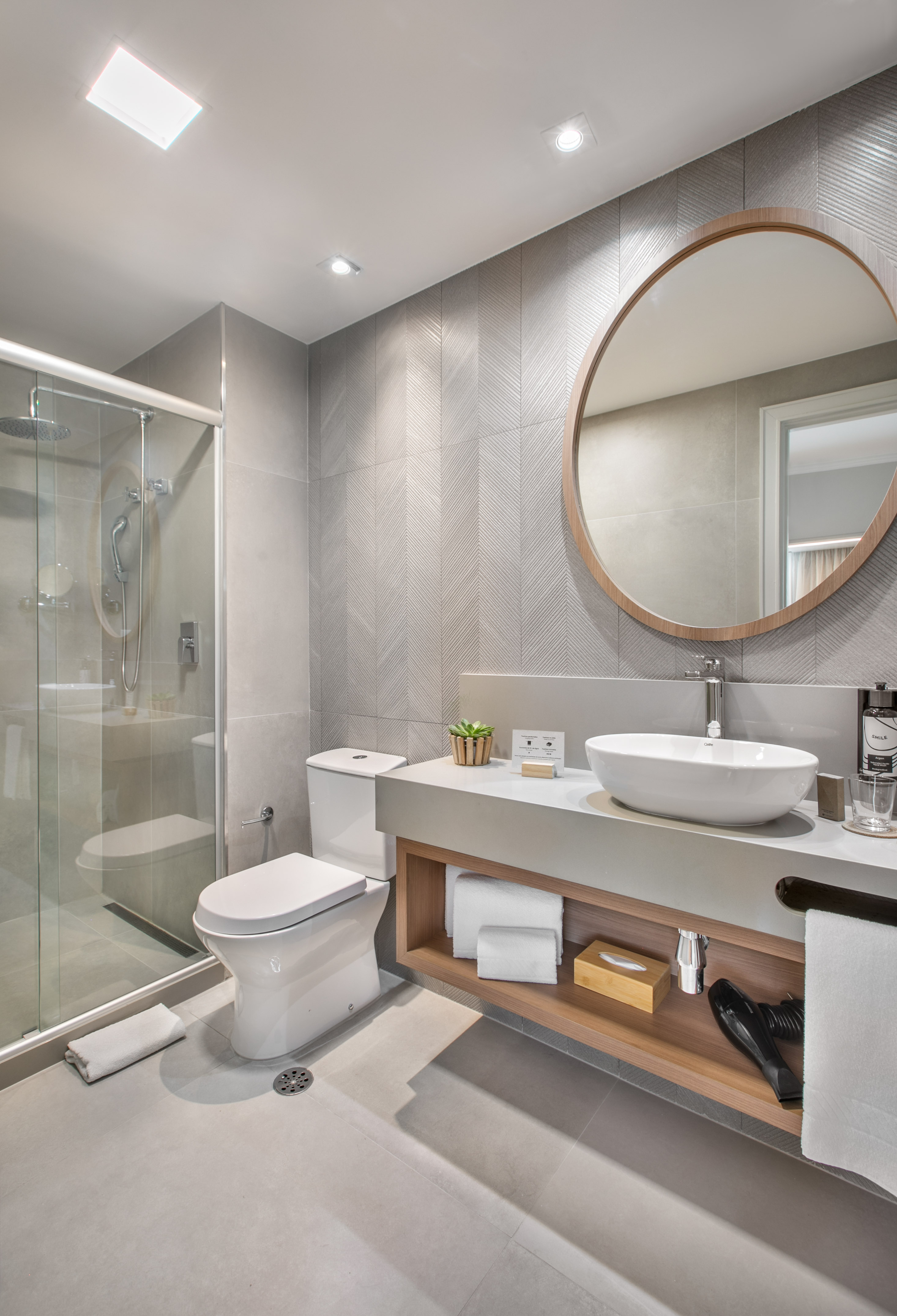 Contemporary hotel bathroom, grey chevron tiles, vessel sink, glass shower.