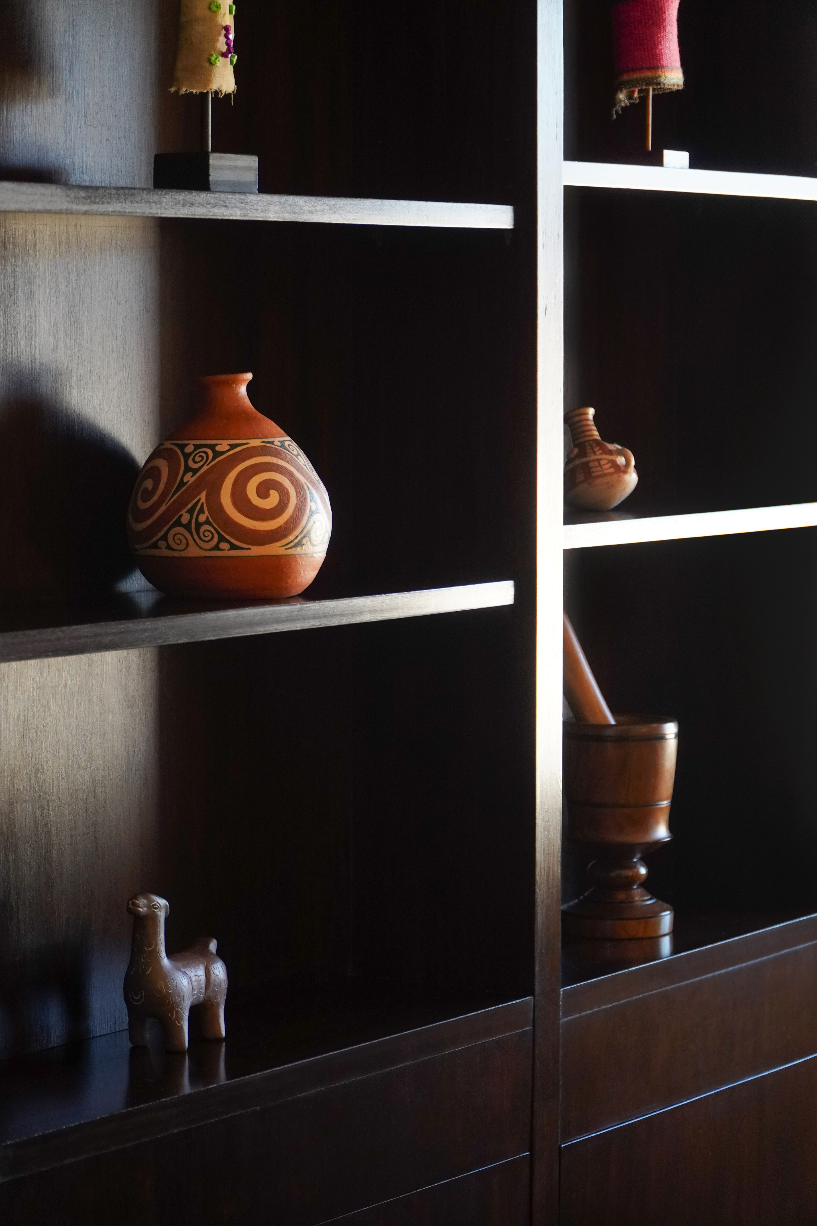 Artisanal terracotta vase with spiral patterns on dark wooden shelves, cultural decor.