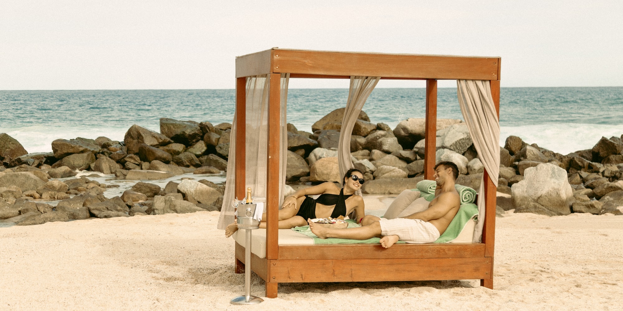a man and woman lying on a bed on a beach