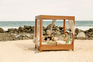 a man and woman lying on a bed on a beach
