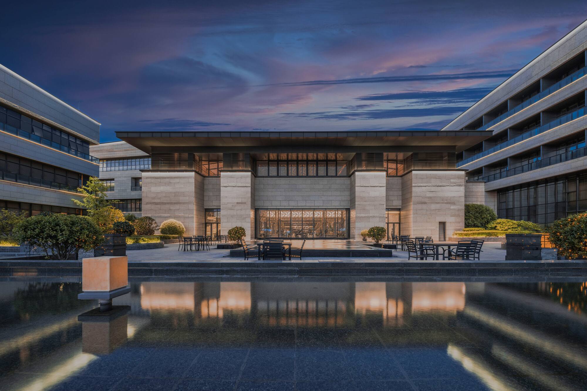Modern building with reflecting pool, outdoor seating, vibrant dusk sky.