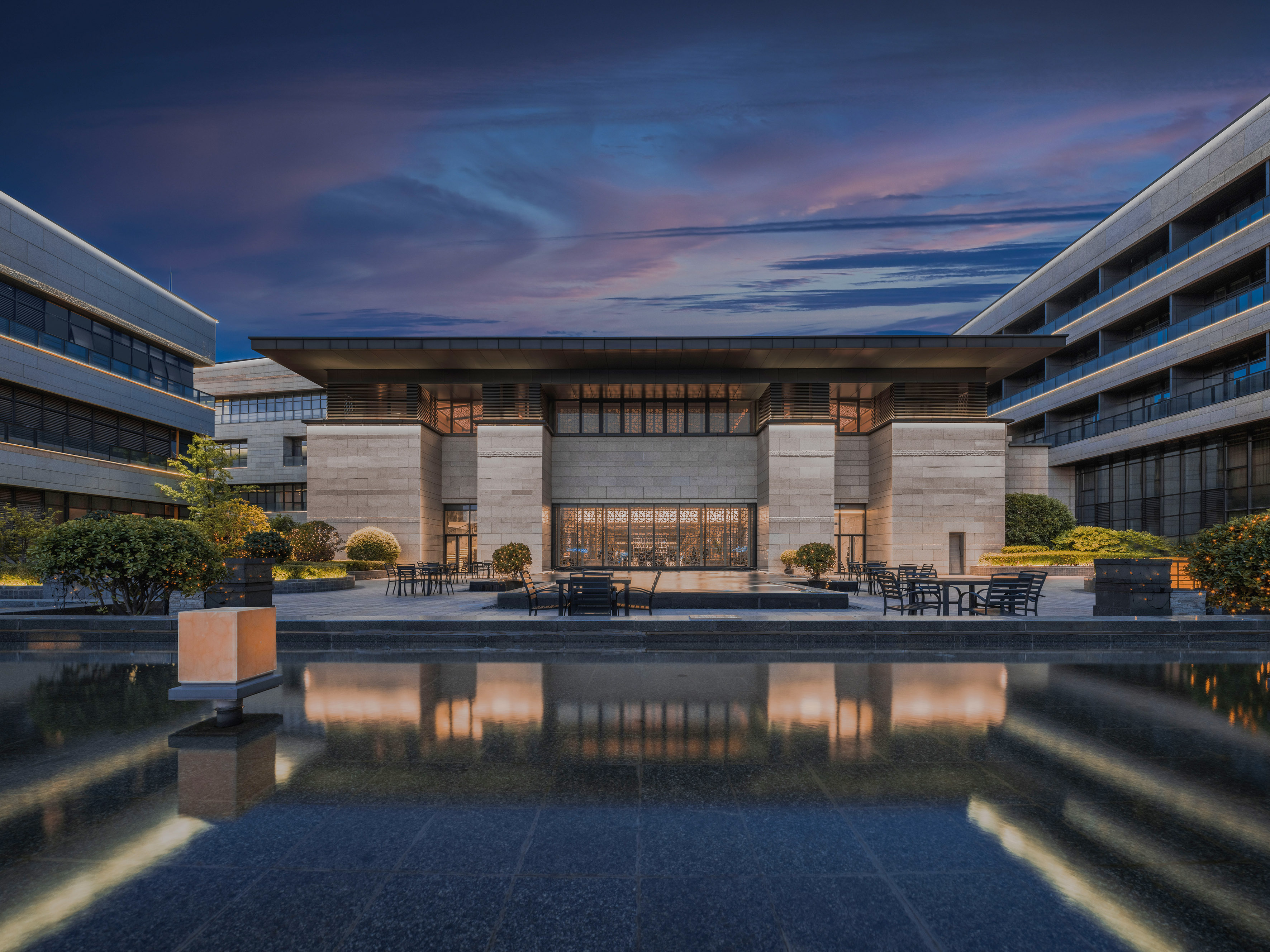 Modern building with reflecting pool, outdoor seating, vibrant dusk sky.