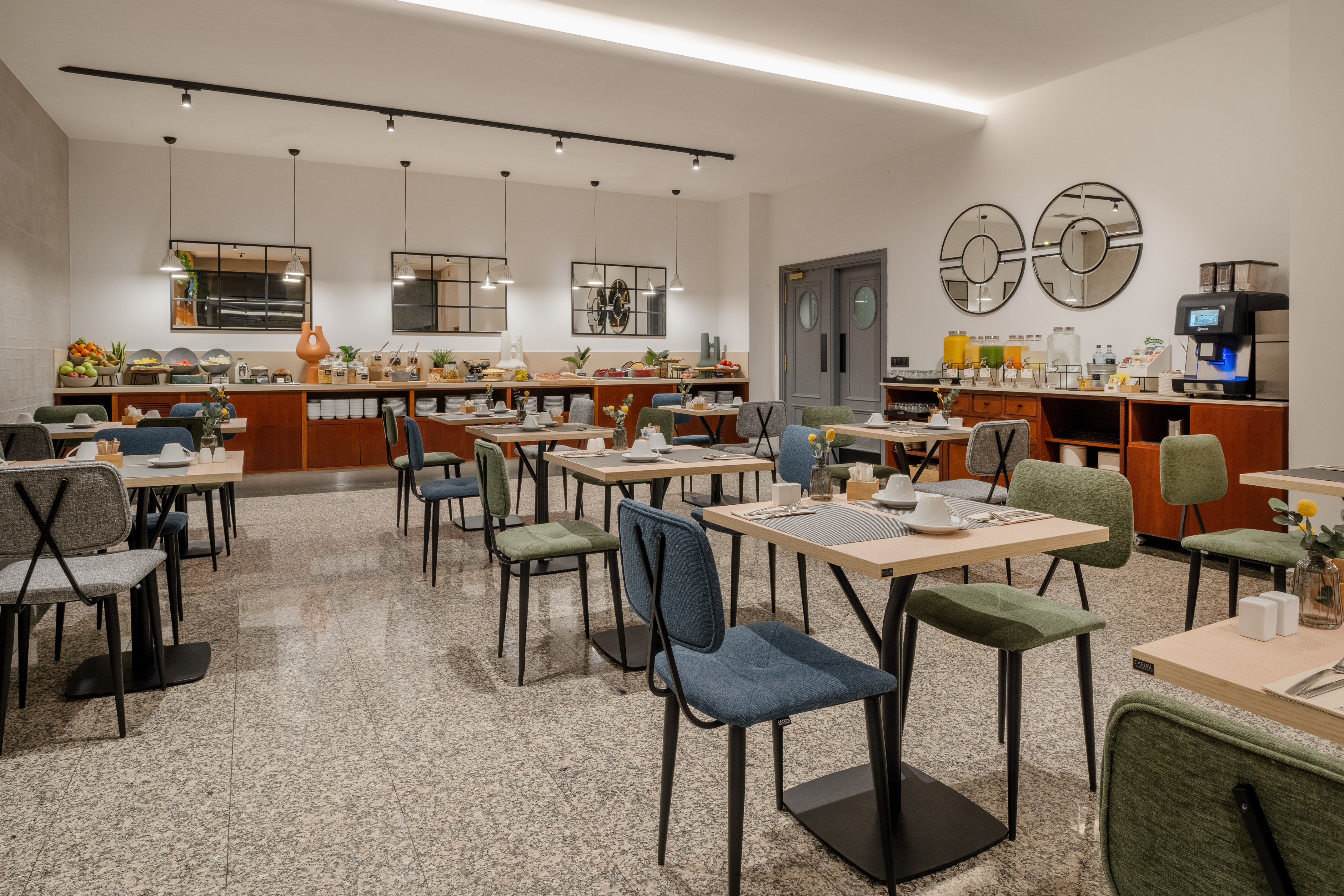 Modern hotel breakfast room with buffet spread and dining tables.