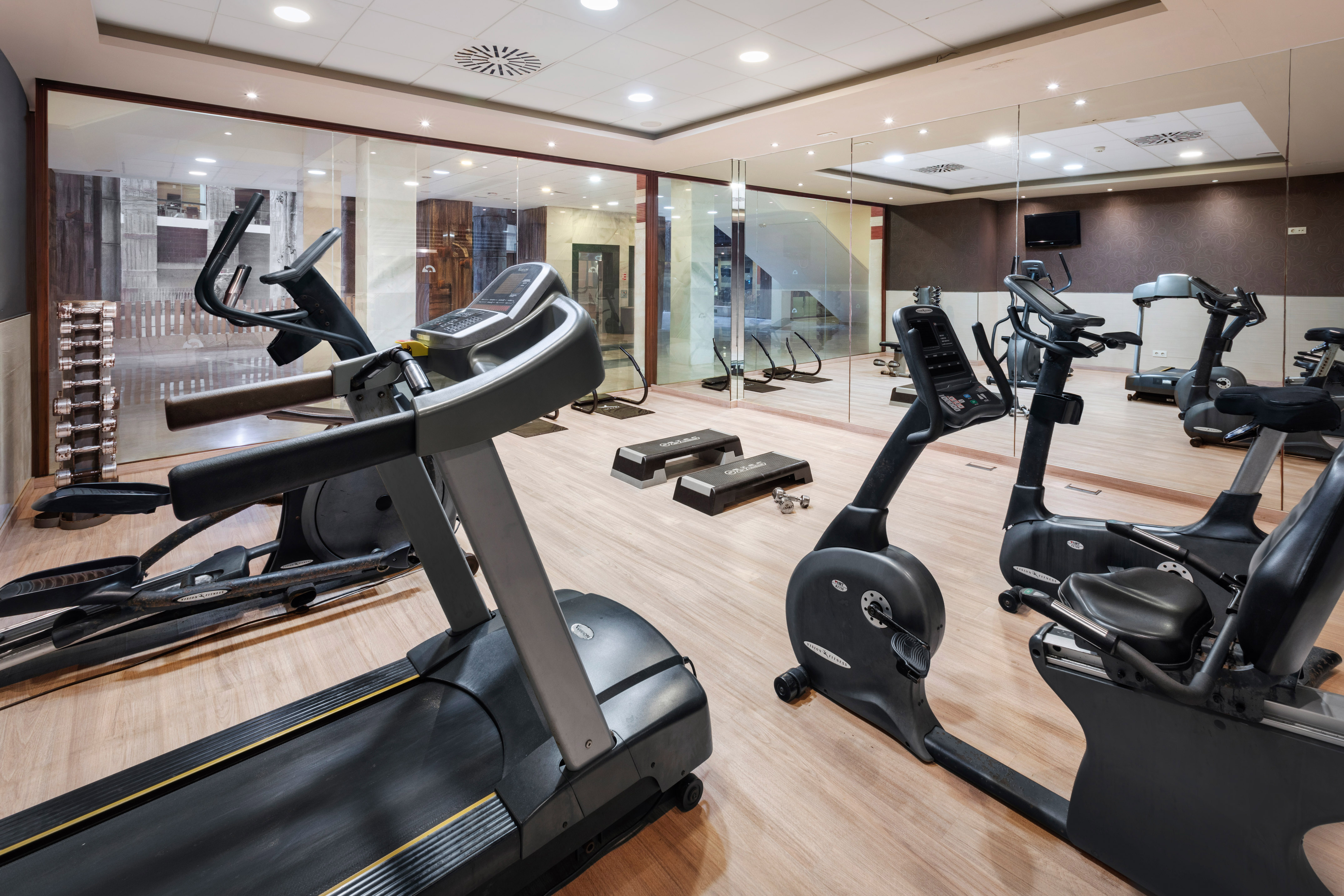 Hotel fitness center with treadmill, elliptical, stationary bikes, and dumbbells.