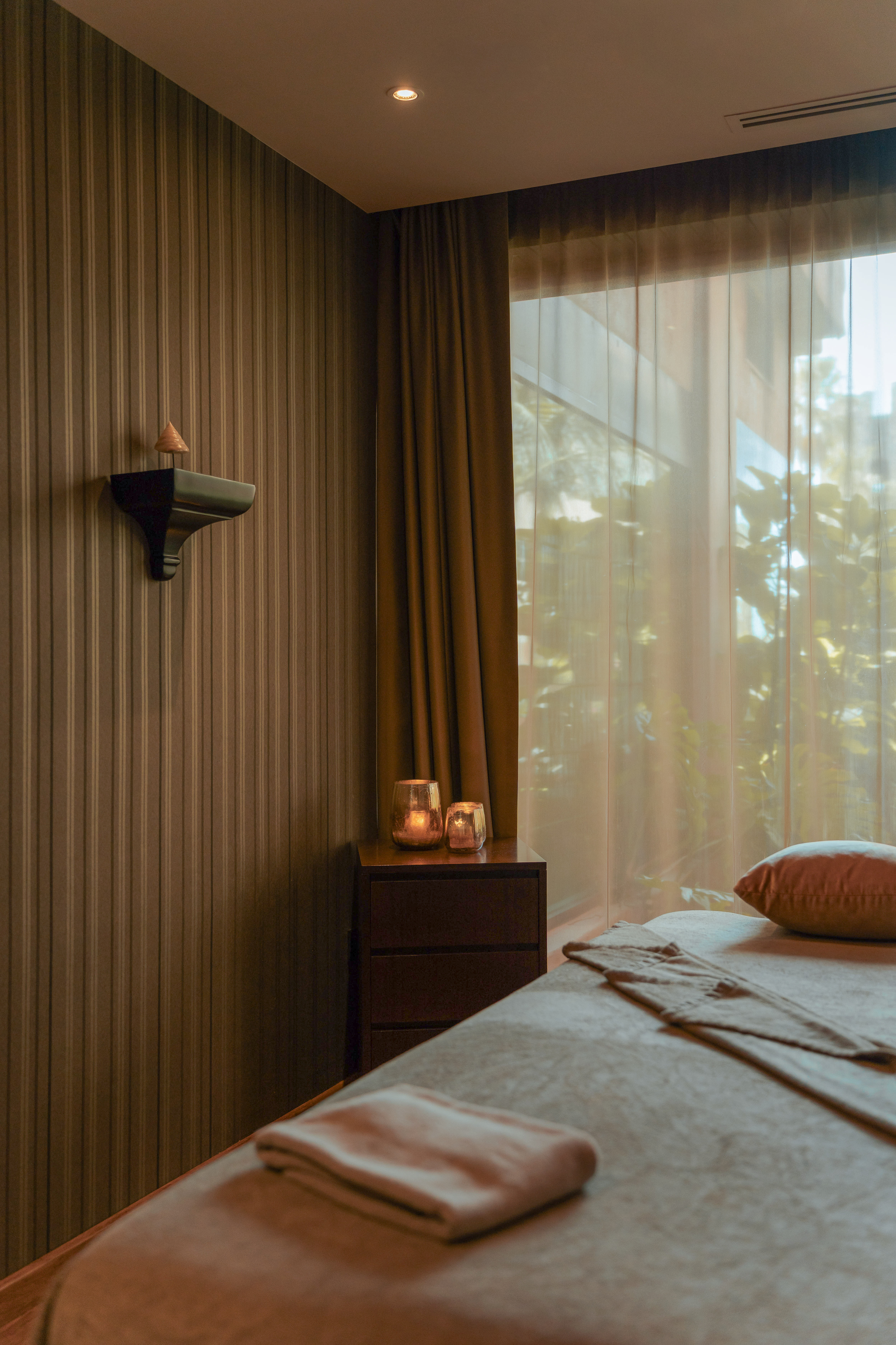 Acogedora sala de spa con mesa de masajes, velas encendidas y luz natural filtrada.