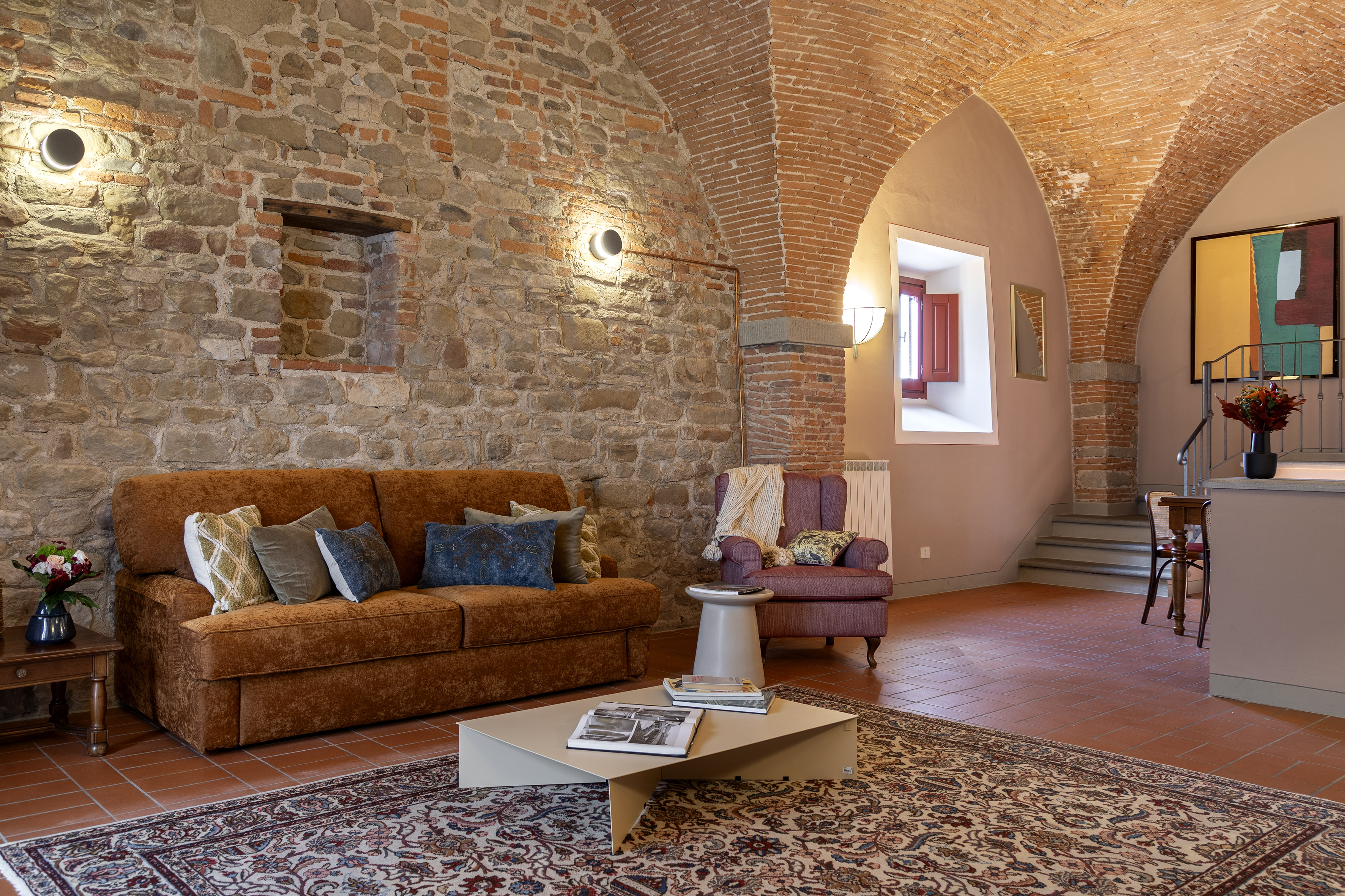 Tuscan living room, stone walls, brick arches, orange sofa, patterned rug.