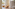 Bichon Frise in pet bed with bowls, "We Dog Care" bag, bright pet-friendly room.