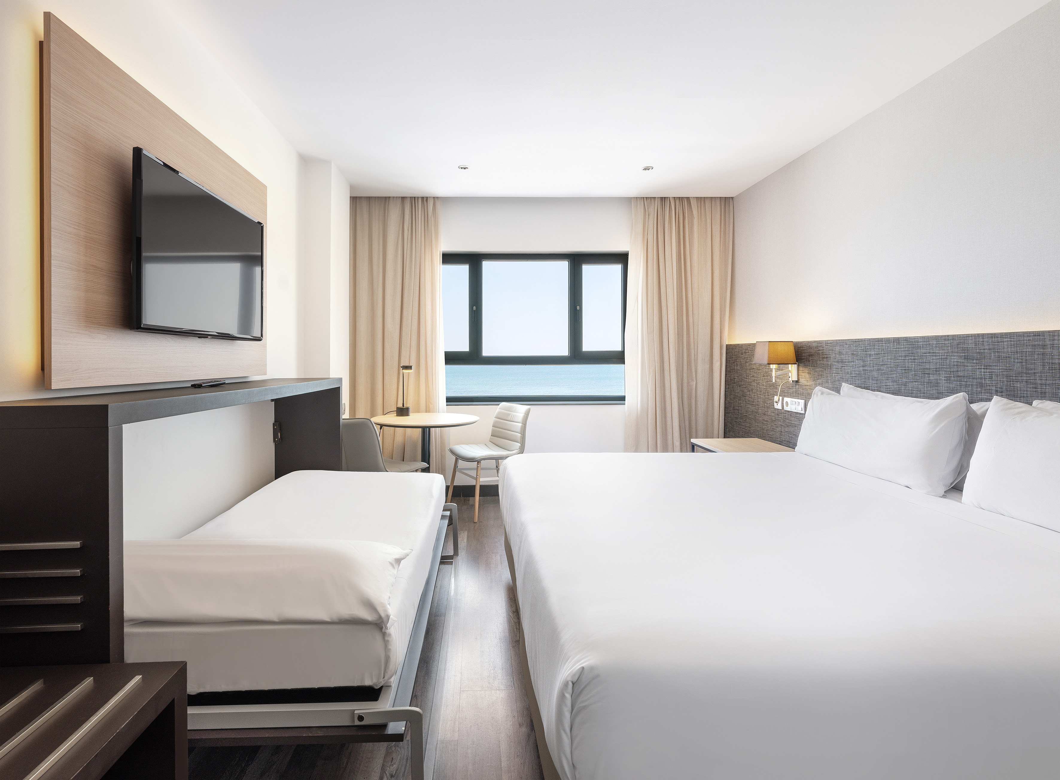 Hotel room with king bed, pull-out bed, TV, and ocean view.