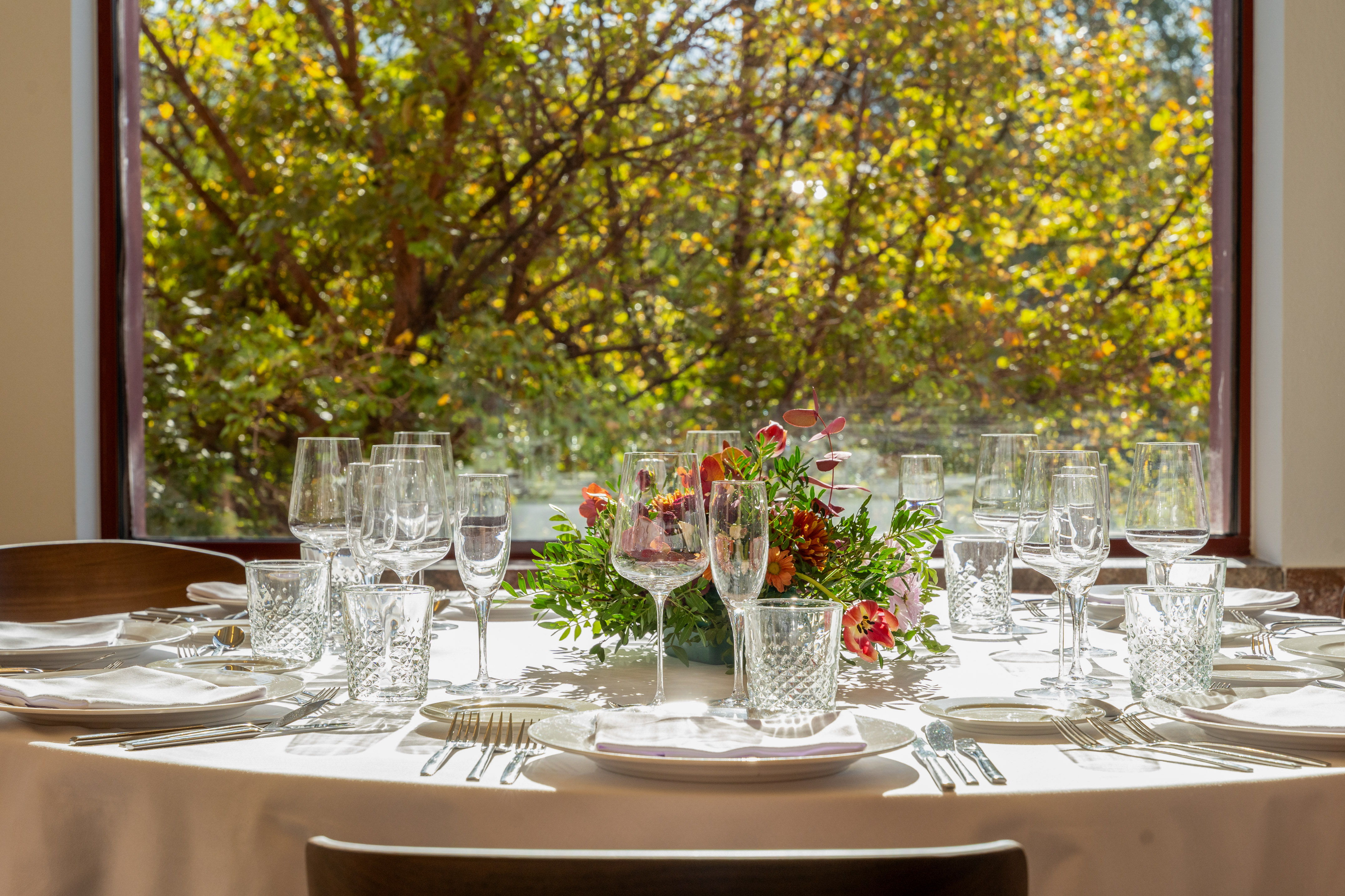 Elegant dining table with place settings, floral centerpiece, sunlit window view.