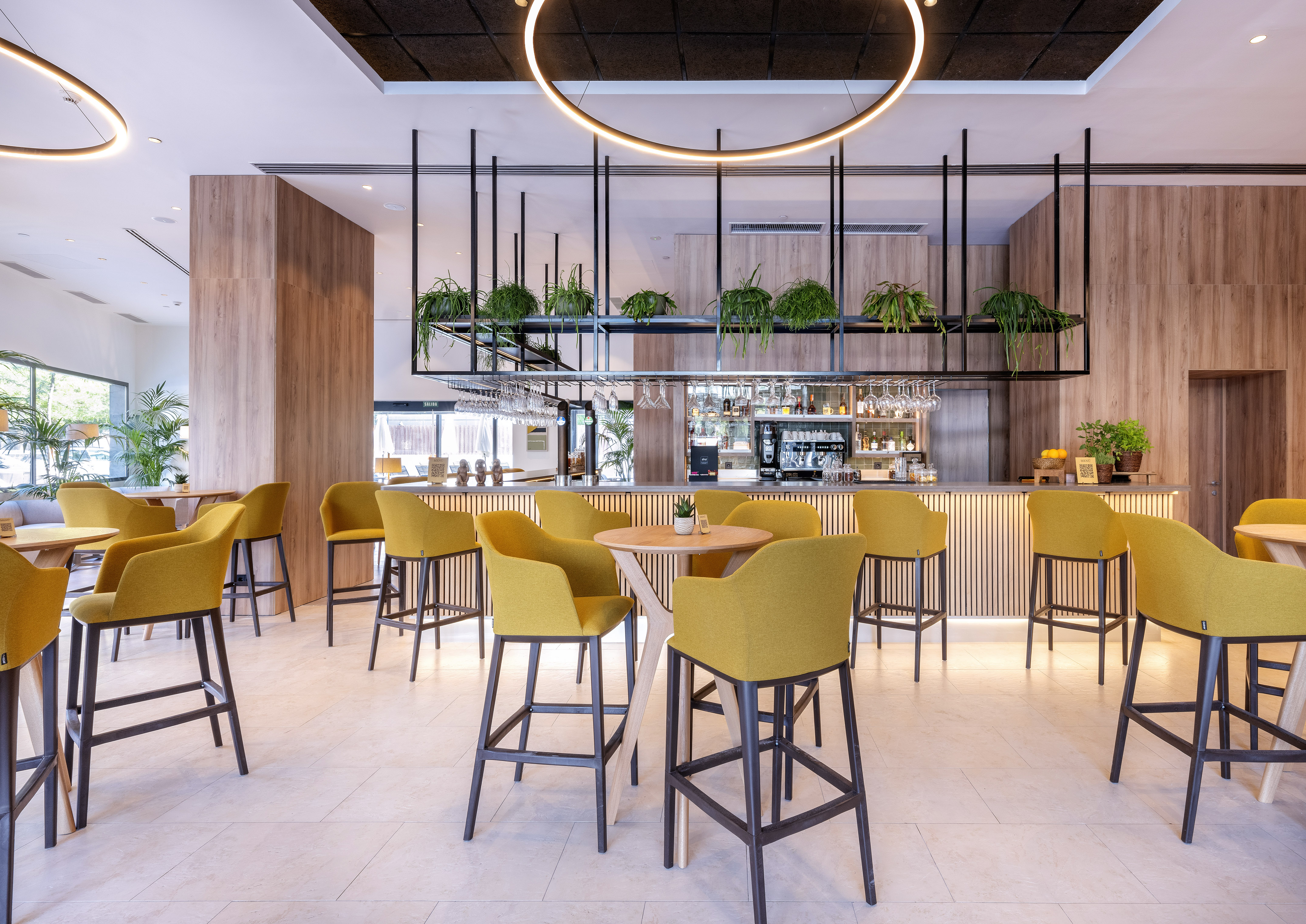 Modern bar lounge with yellow stools, wood accents, and hanging plants.