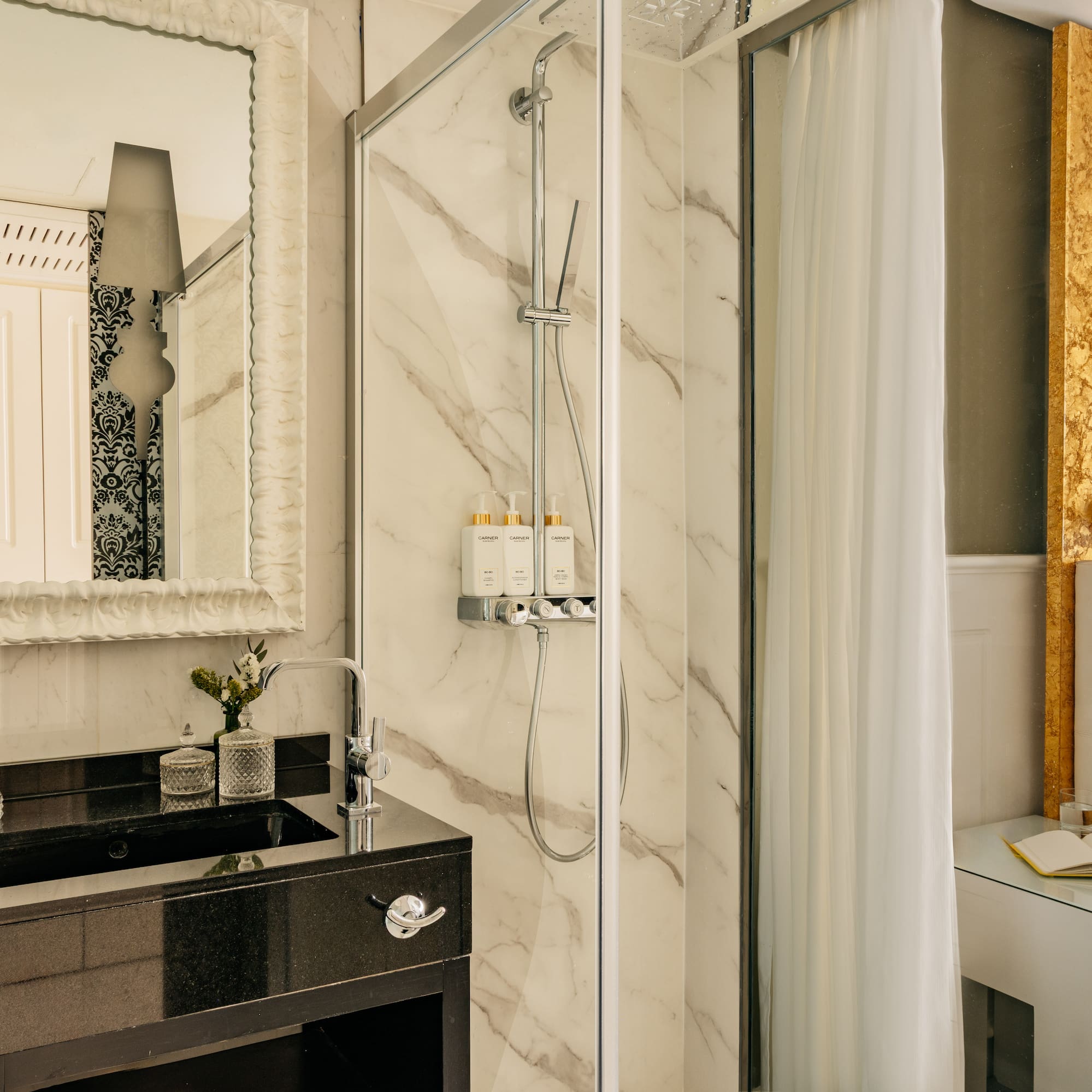 Lujosa suite de hotel con baño de mármol, ducha y cabecero dorado.
