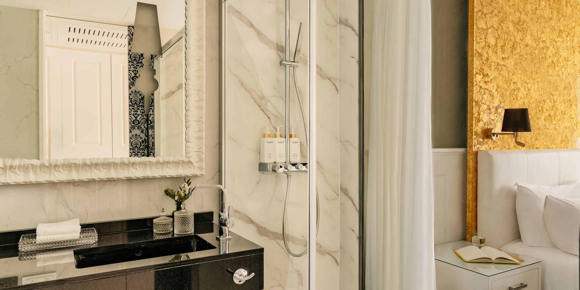Lujosa suite de hotel con baño de mármol, ducha y cabecero dorado.