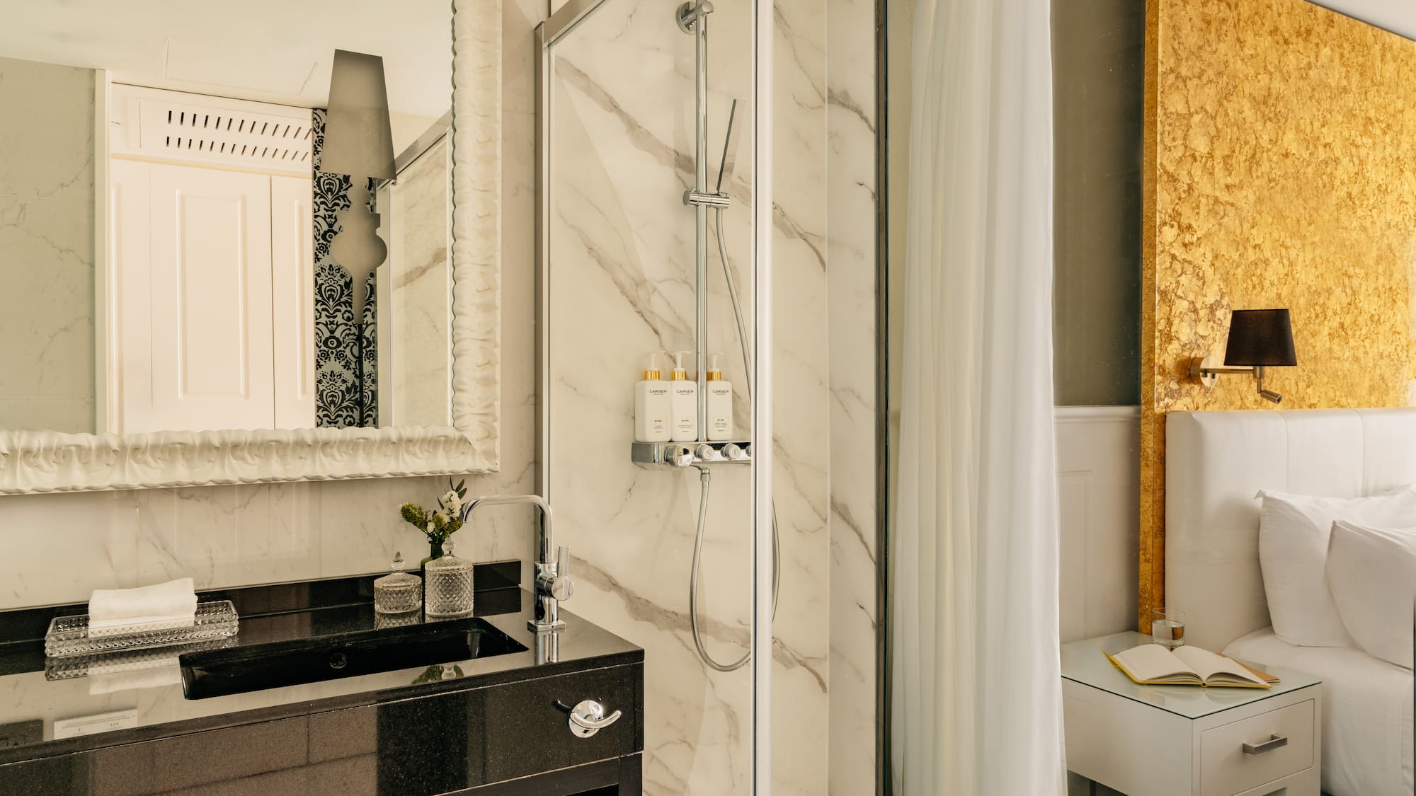 Lujosa suite de hotel con baño de mármol, ducha y cabecero dorado.