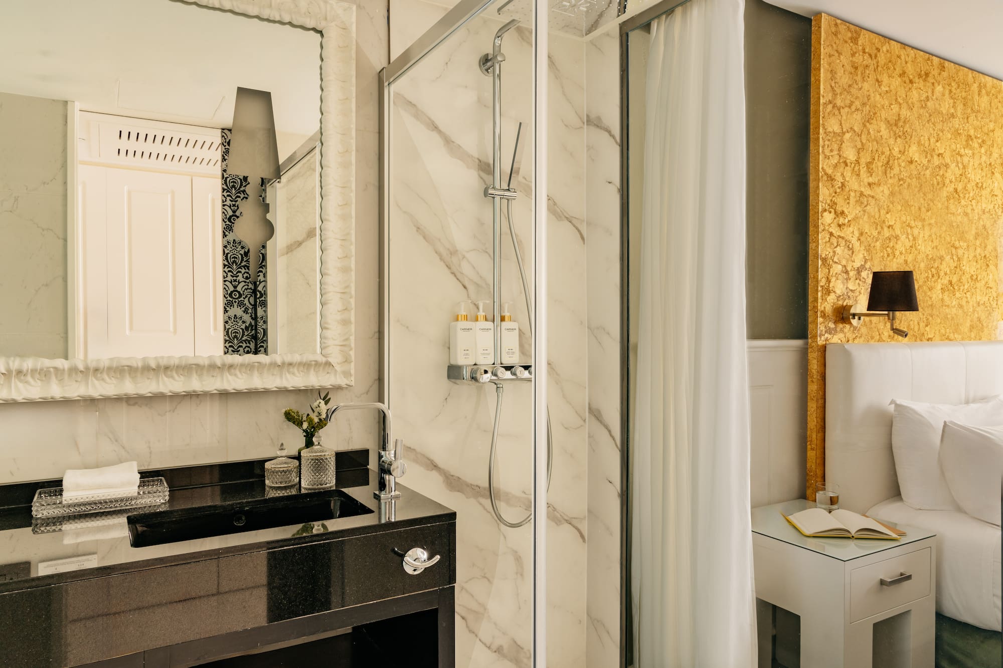 Lujosa suite de hotel con baño de mármol, ducha y cabecero dorado.