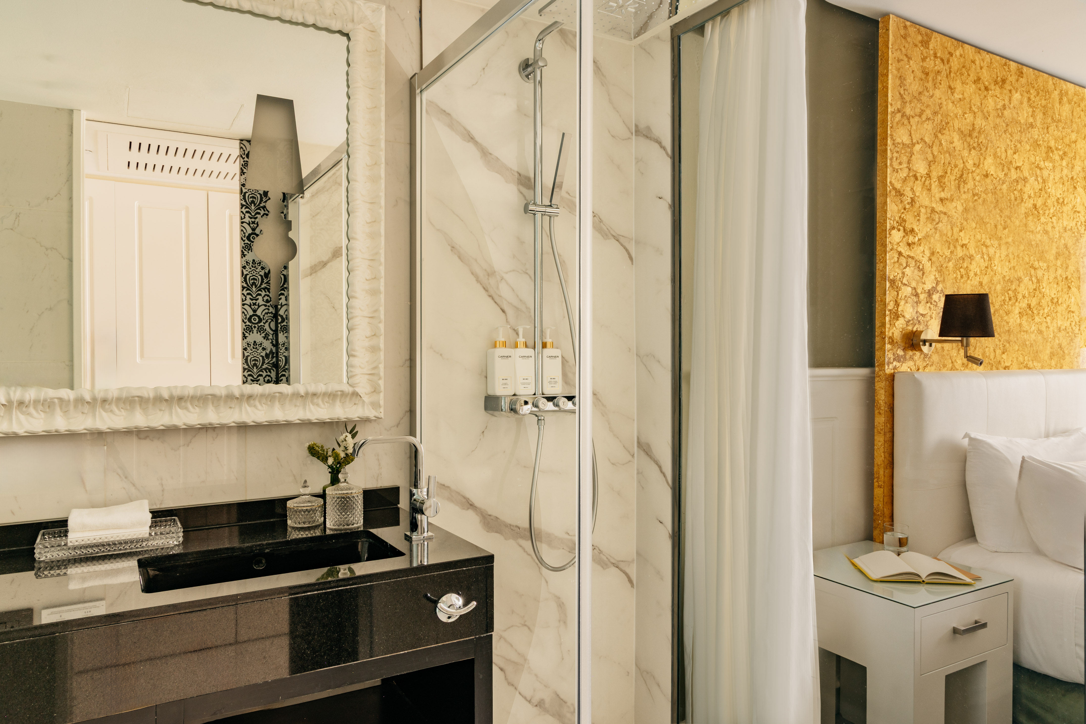 Lujosa suite de hotel con baño de mármol, ducha y cabecero dorado.