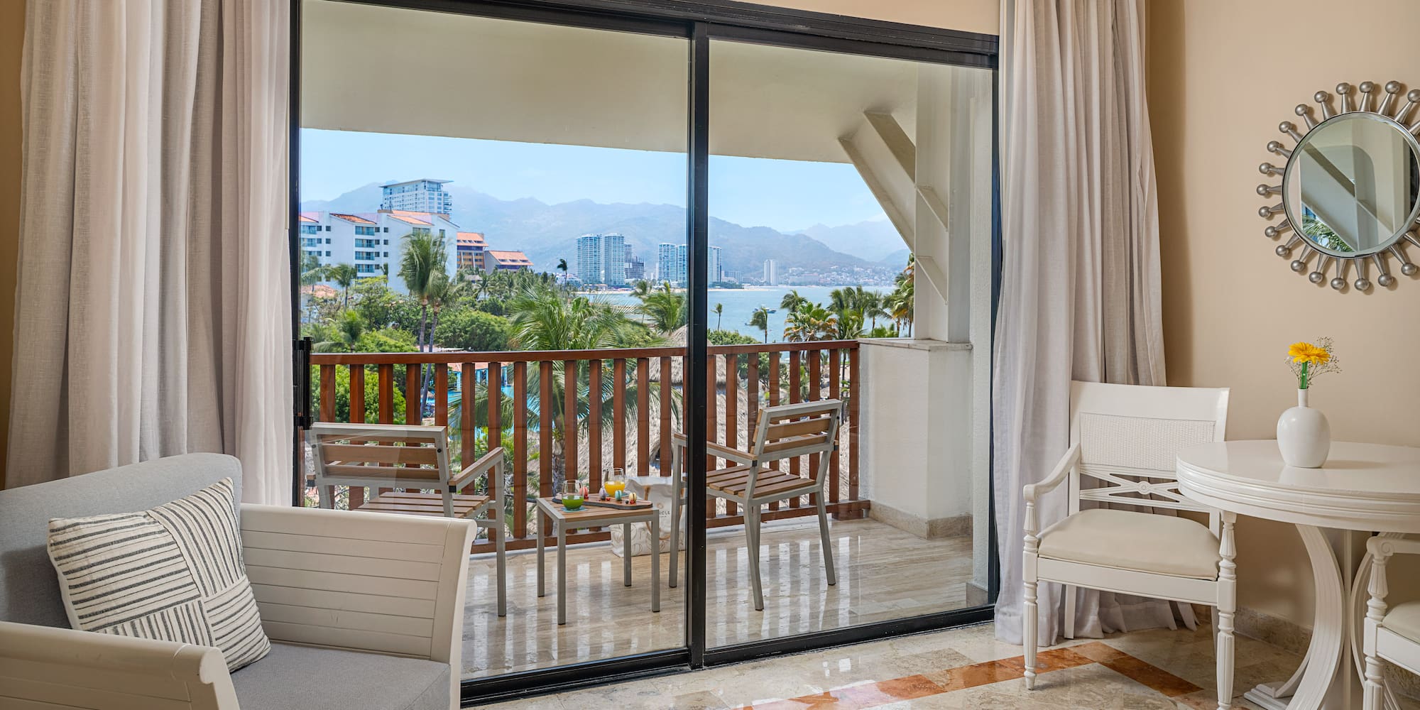 Resort hotel room with private balcony, ocean bay view, palm trees, and city.