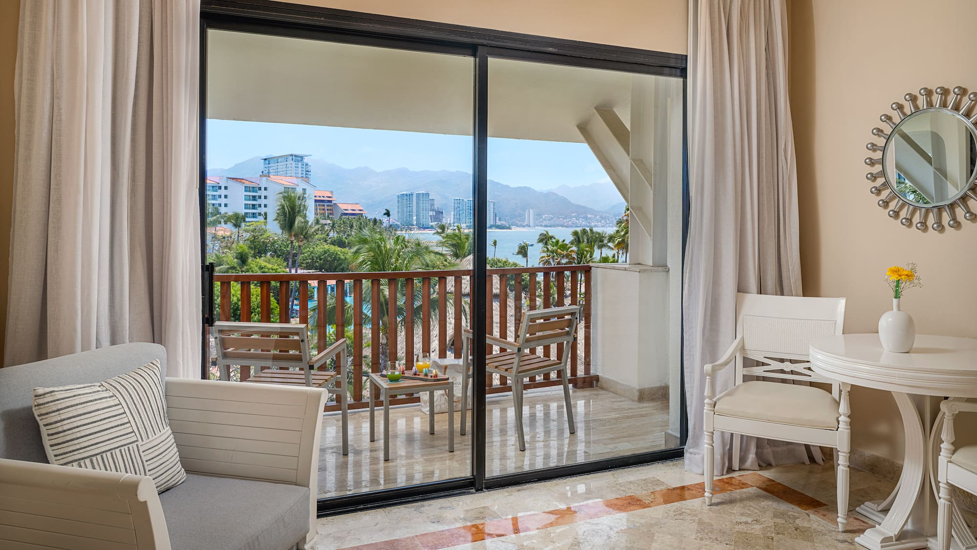 Resort hotel room with private balcony, ocean bay view, palm trees, and city.