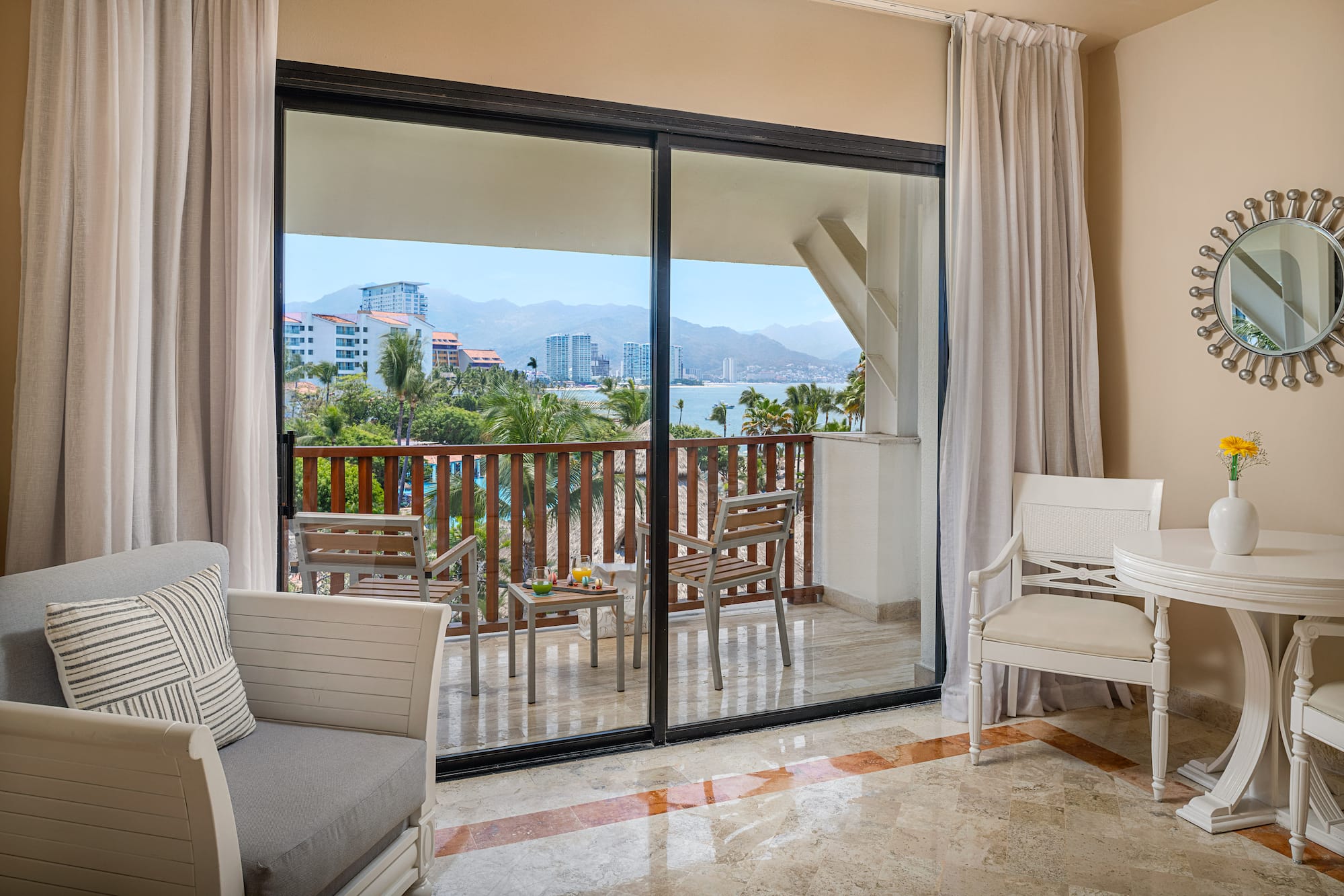 Tropical hotel room balcony with ocean, mountain, and city views.