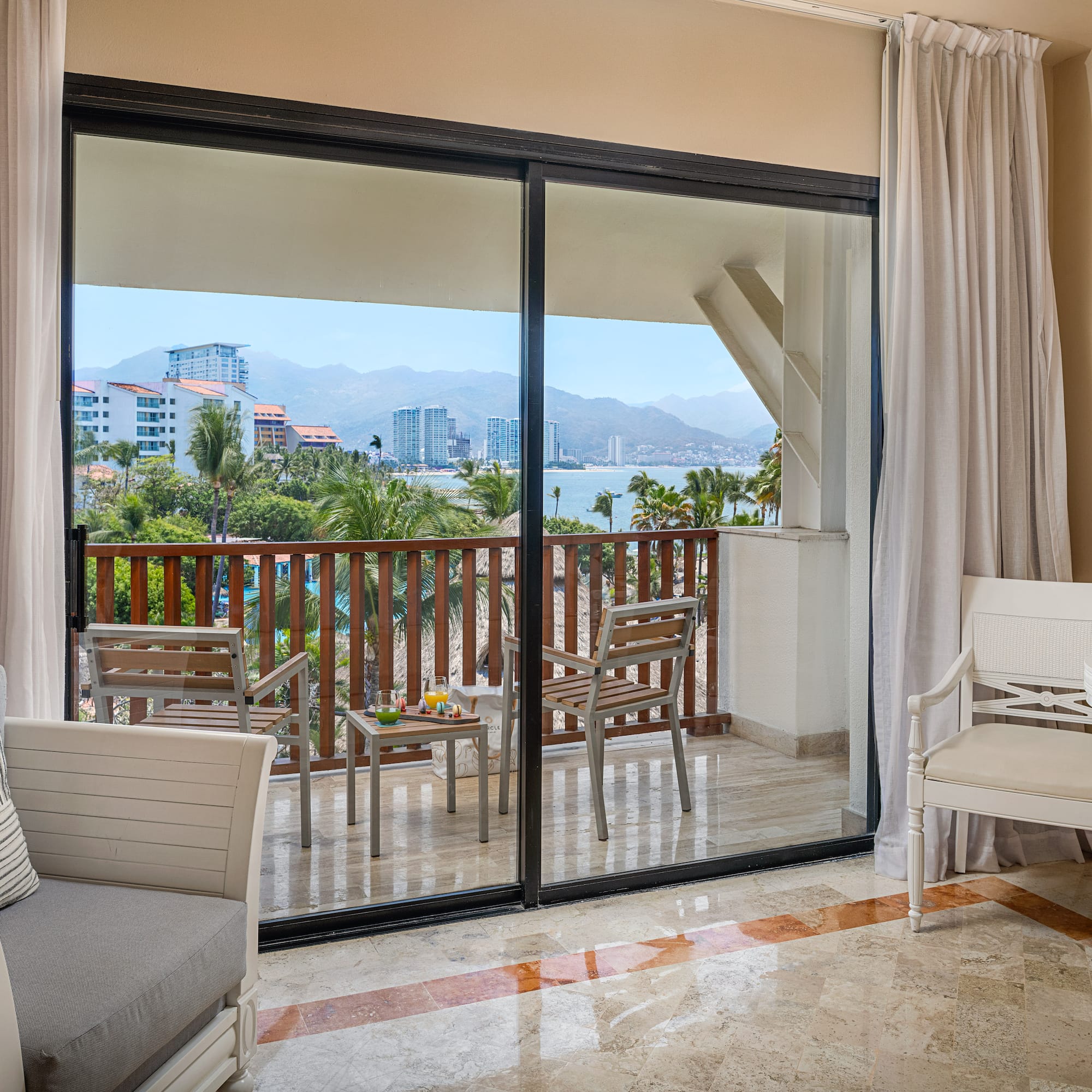 Resort hotel room with private balcony, ocean bay view, palm trees, and city.
