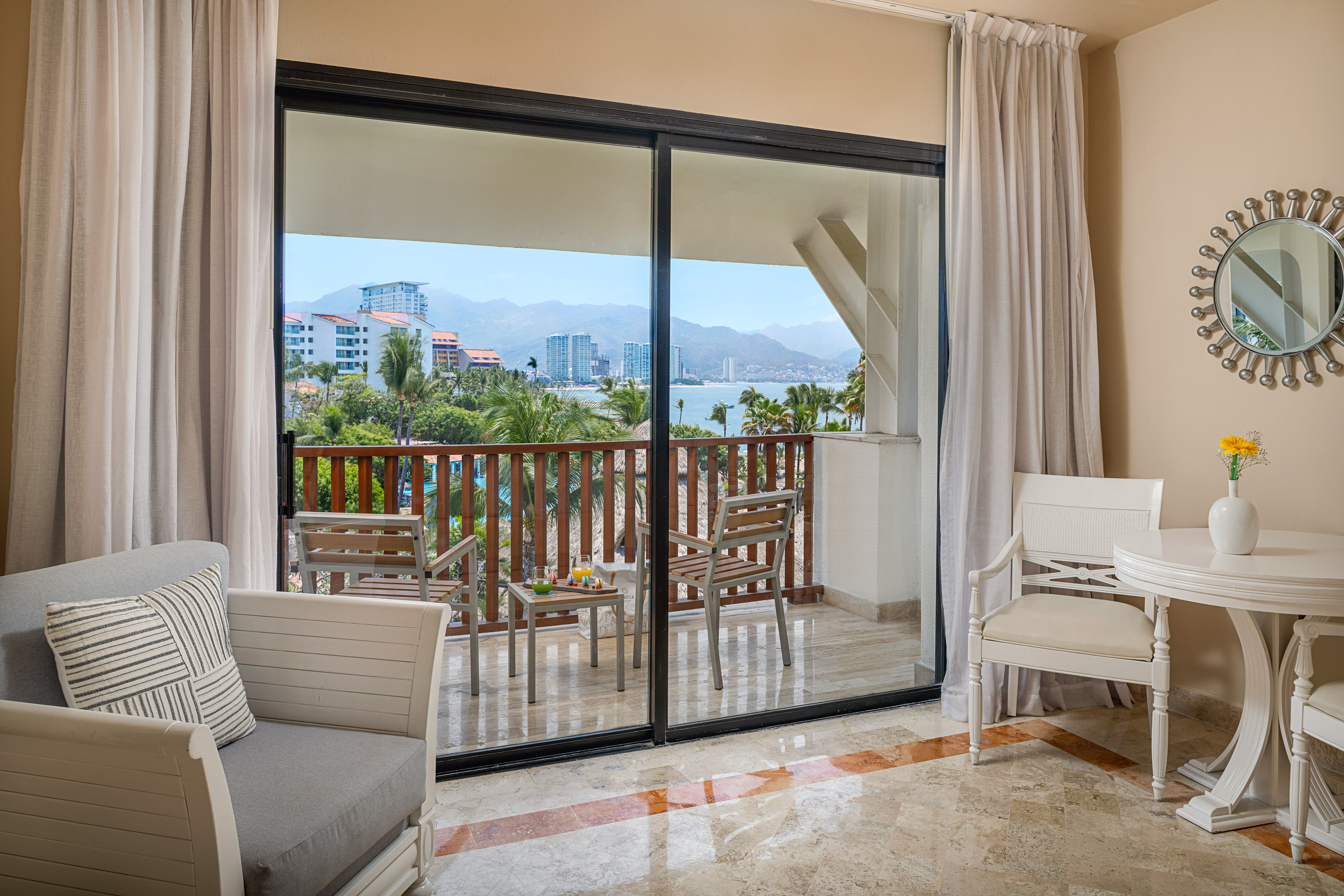 Tropical hotel room balcony with ocean, mountain, and city views.