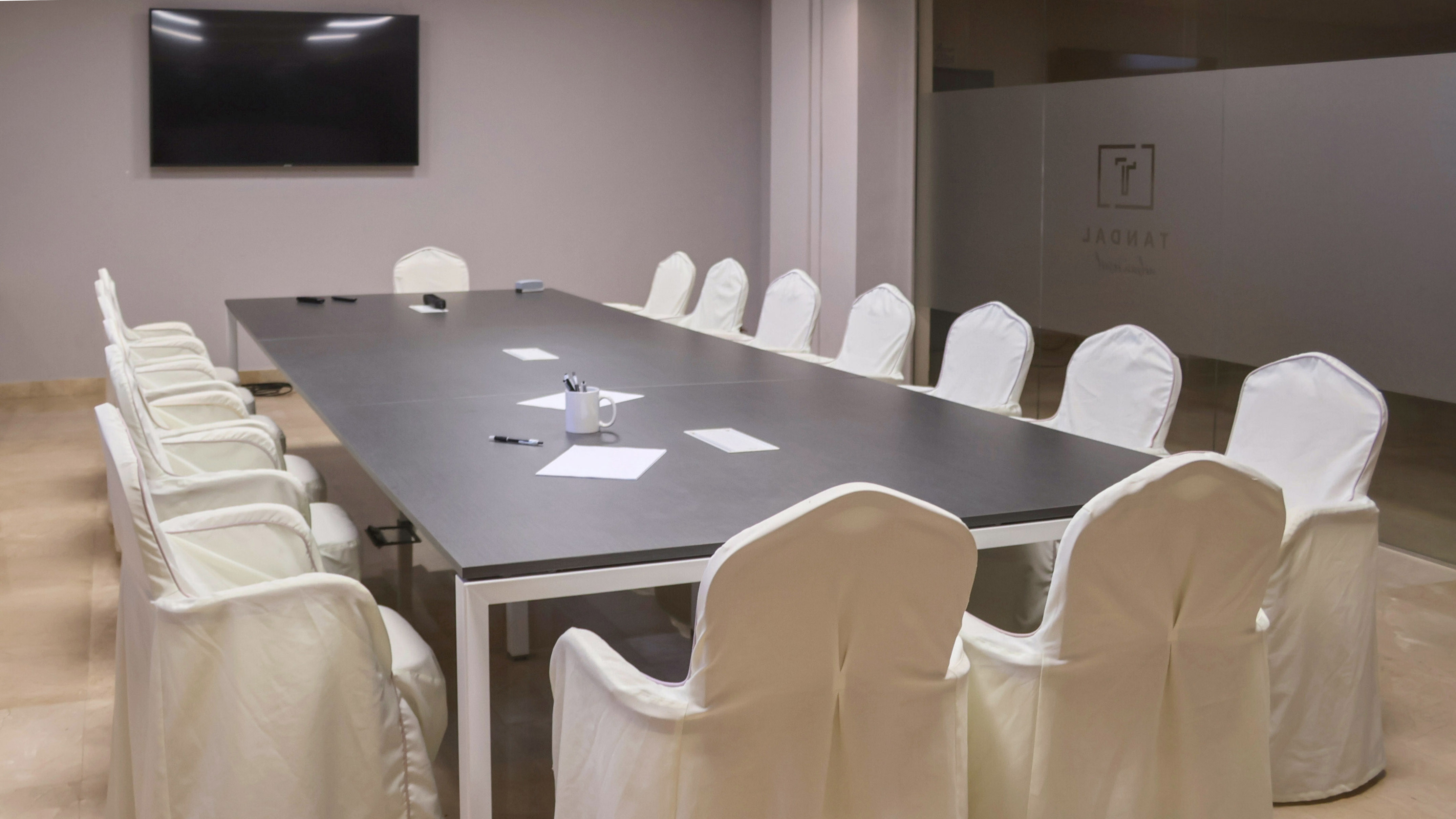 Modern conference room with long dark table, white chairs, and presentation screen.