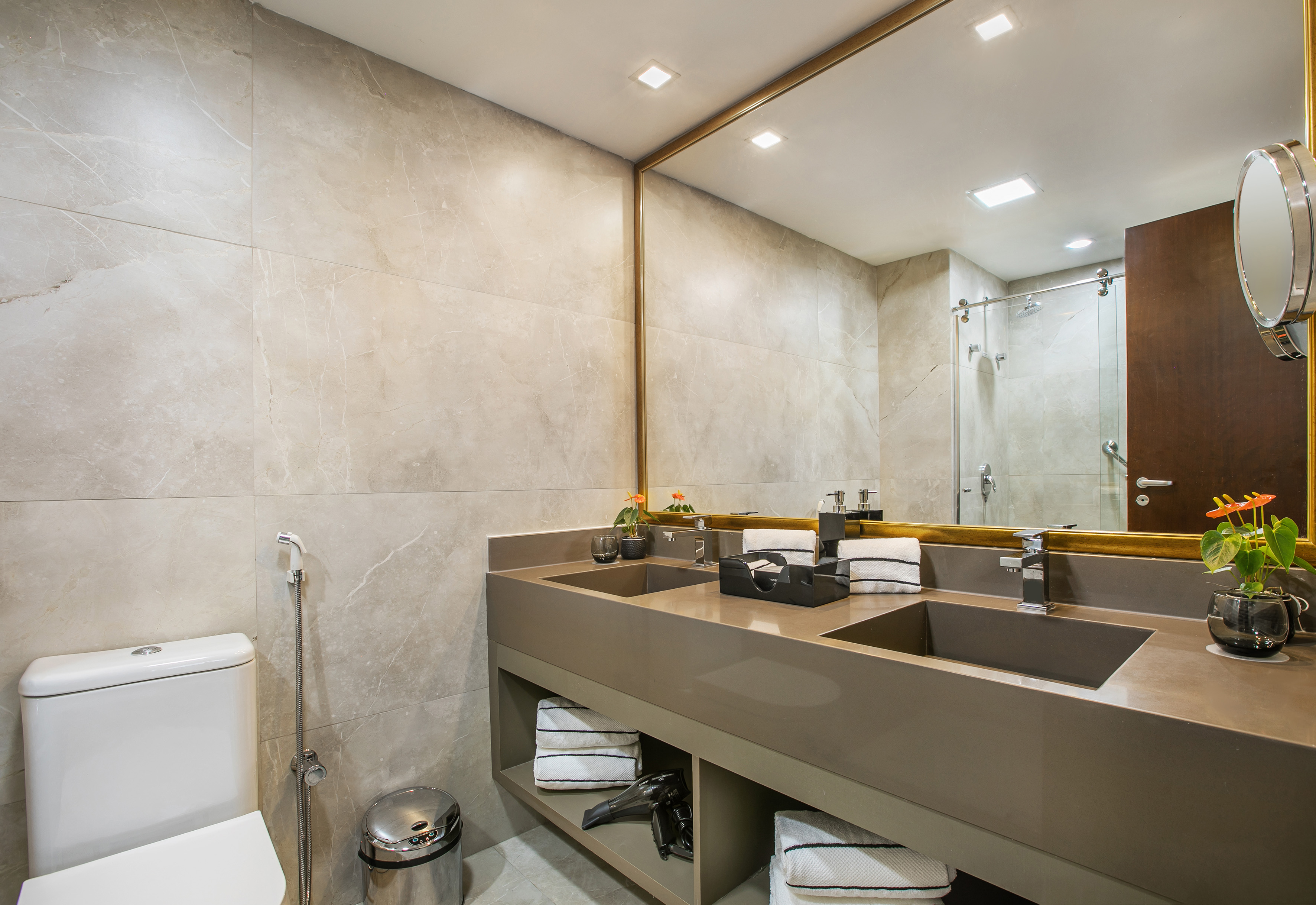 Modern bathroom with dual sink vanity, gold mirror, and grey marble tiles.