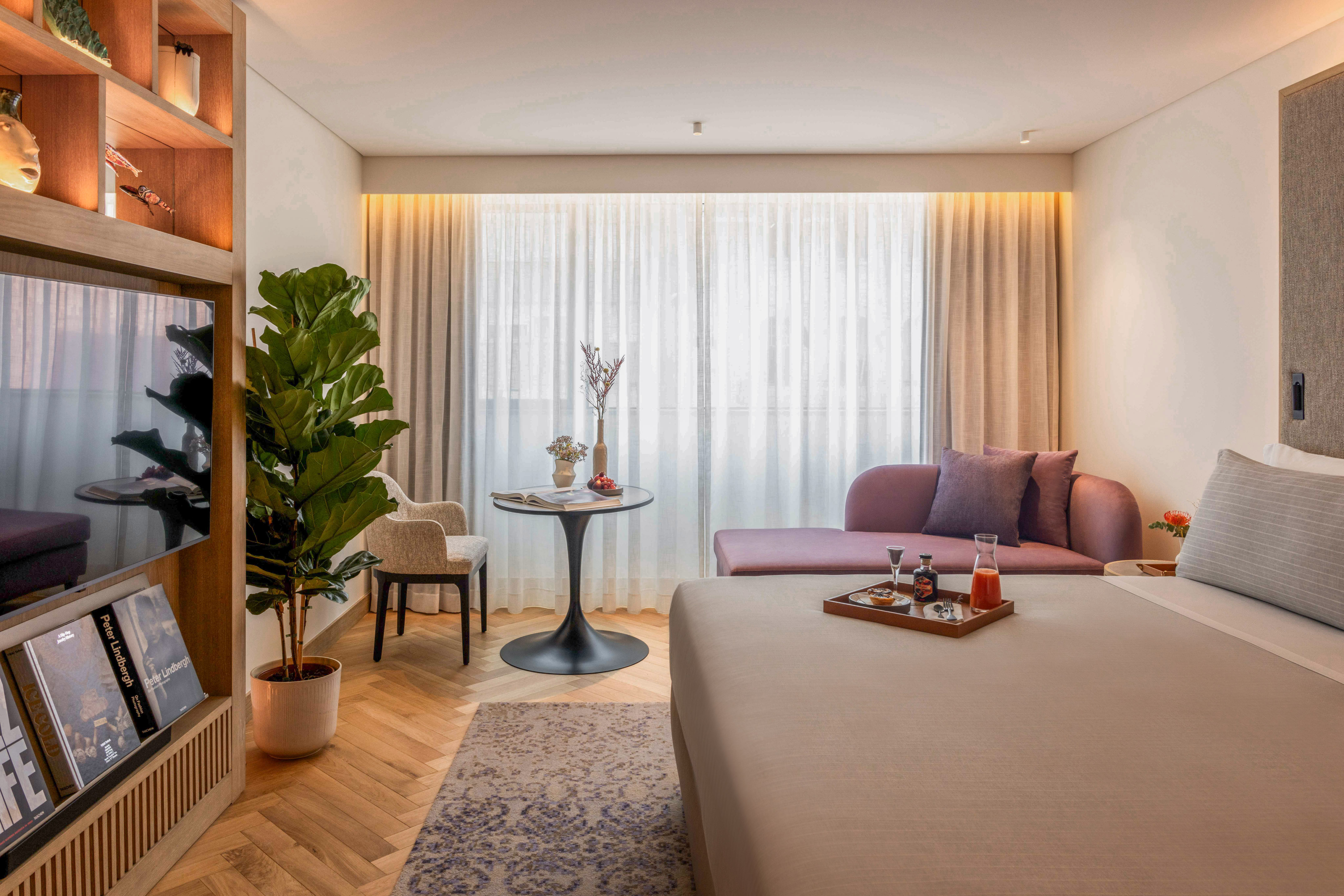 Bright modern hotel suite with bed, lounge, and elegant wood floor.