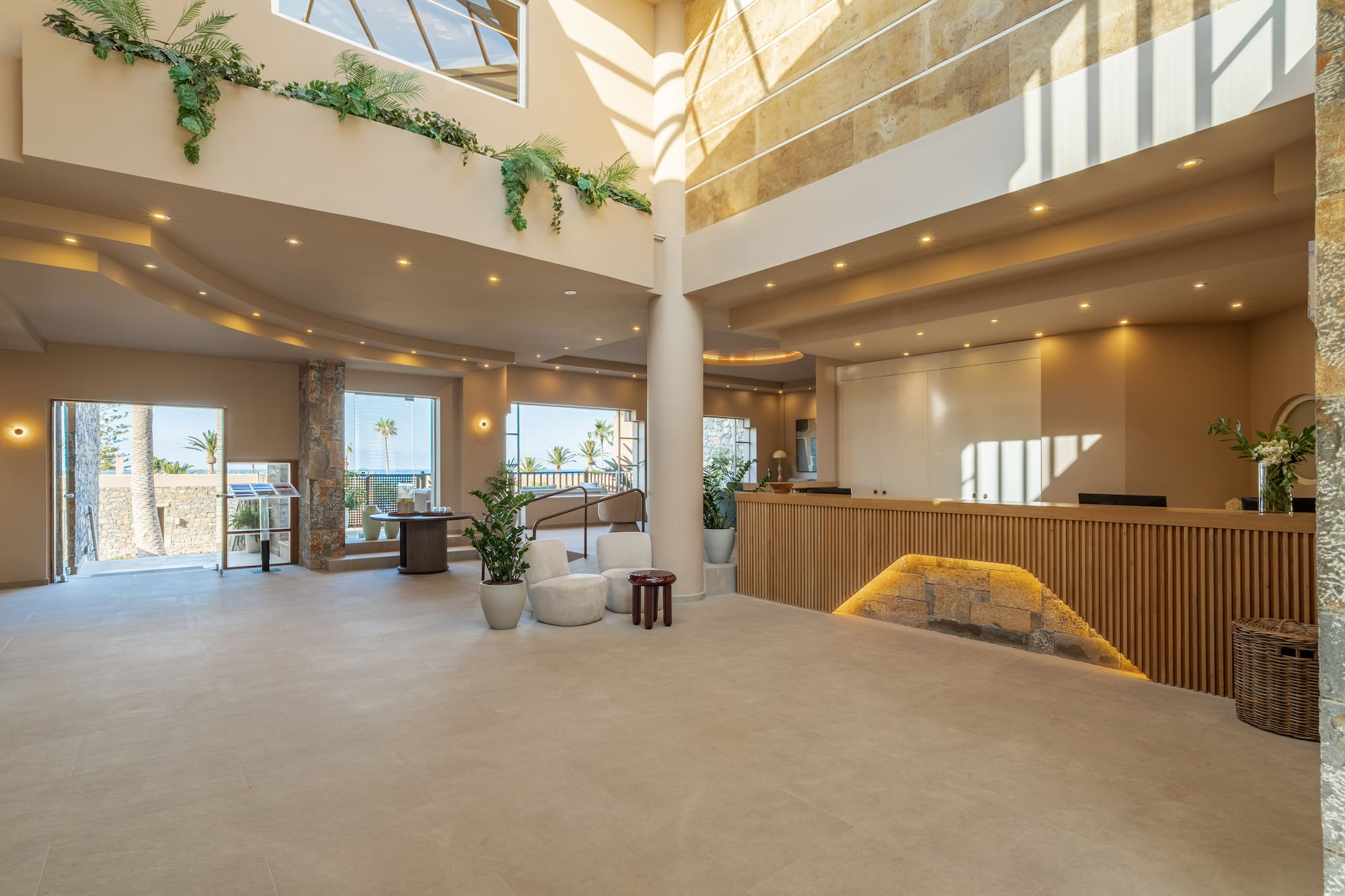 Bright hotel lobby with sea view, modern reception desk, and lush plants.
