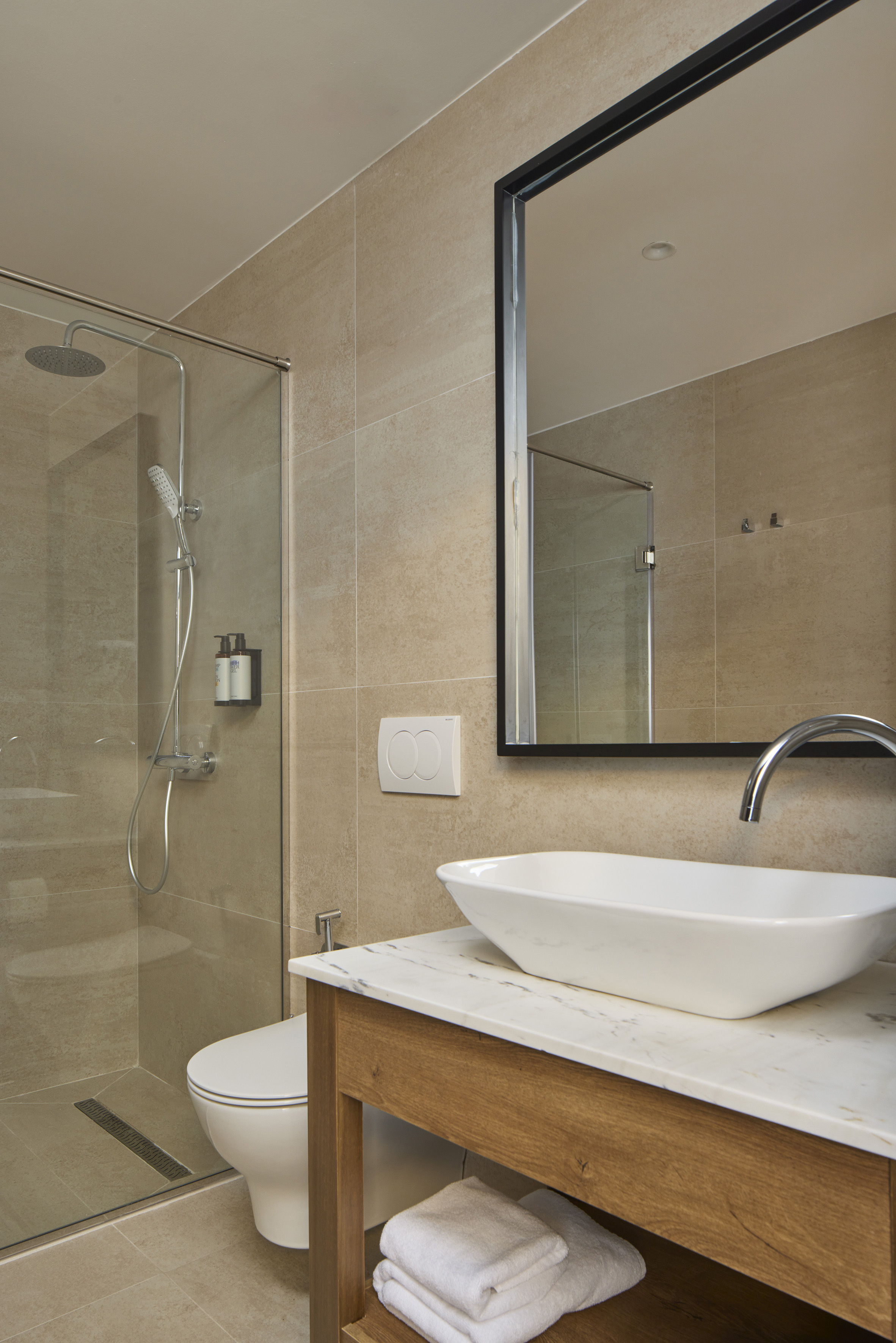 Modern beige bathroom with glass shower, toilet, and vessel sink.