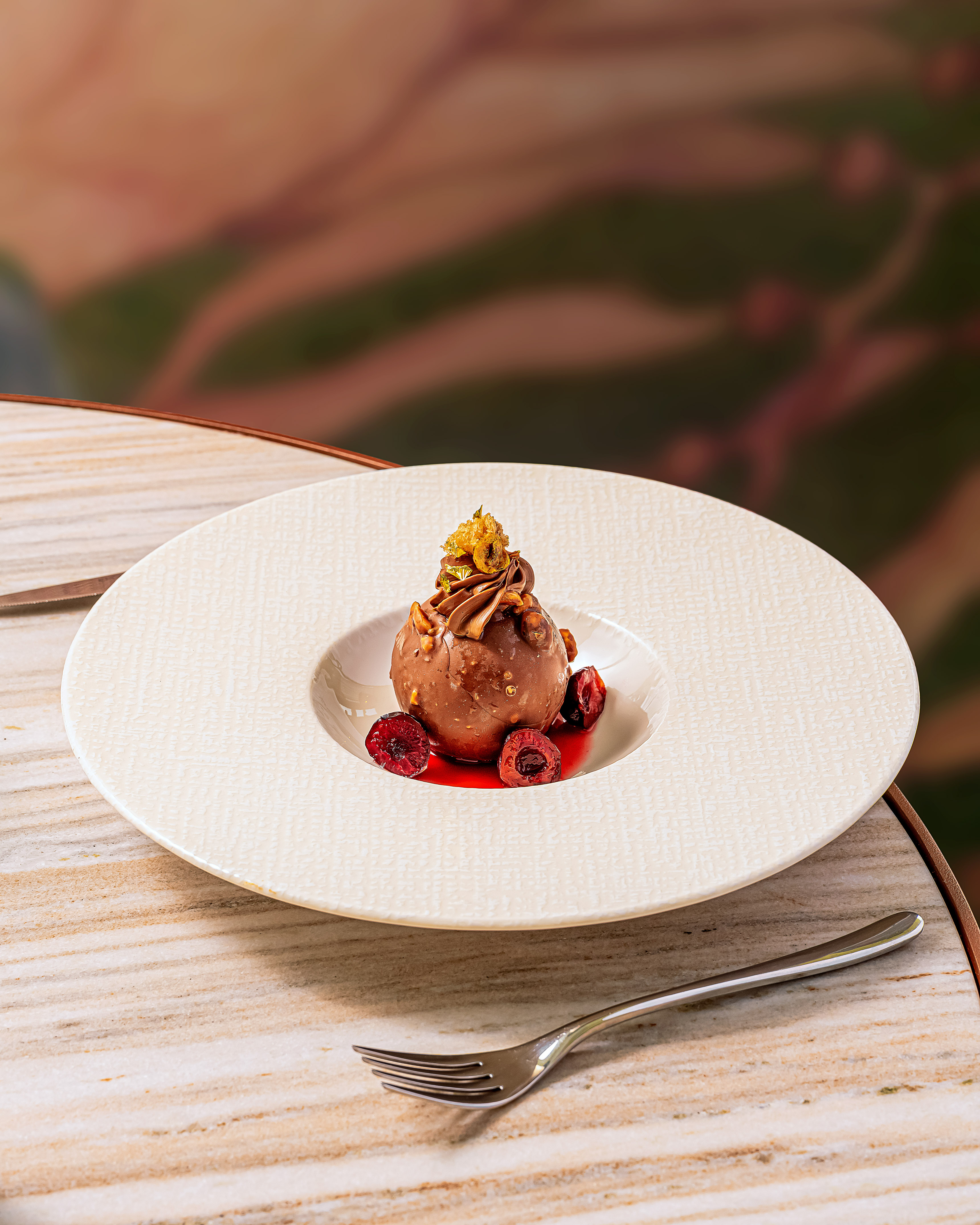 Gourmet chocolate hazelnut dessert with cherries, gold leaf, and cherry sauce.