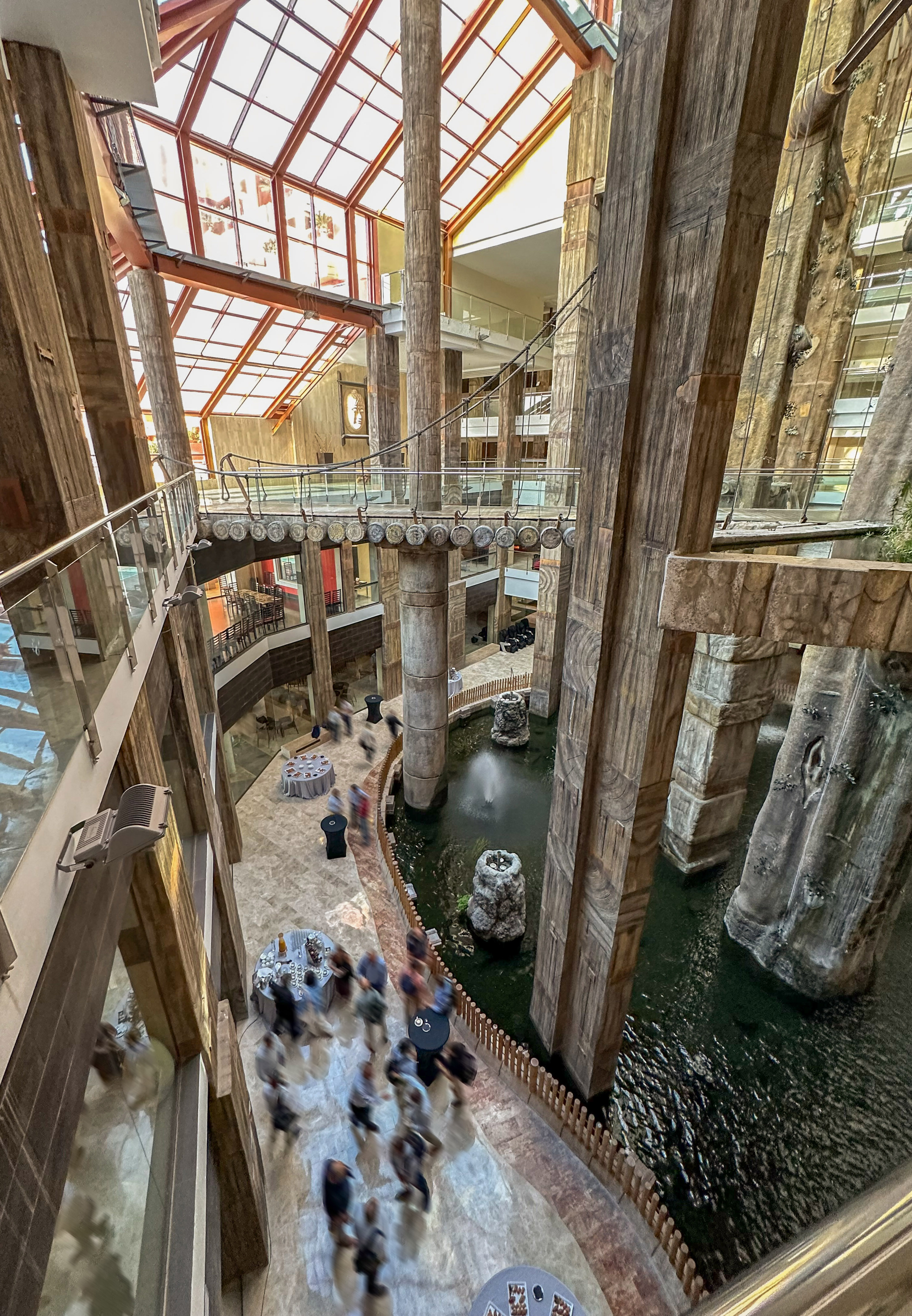 Atrium with large textured pillars, water feature, glass roof, and people.